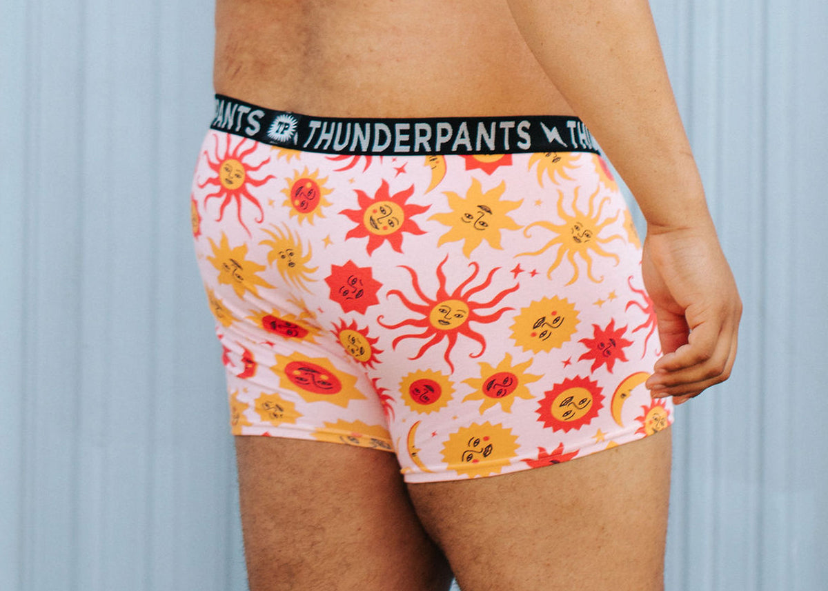 Model wearing Thunderpants Boxer Brief style underwear in Luna y Sol Print - pink with red and orange suns and moons.