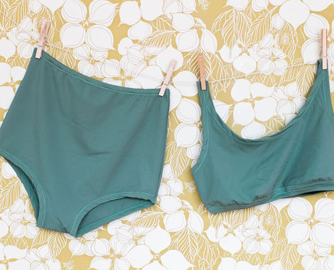 Thunderpants Sky Rise Bottoms and Top Swimwear in Lichen Green hanging by clothes pins on a floral background.