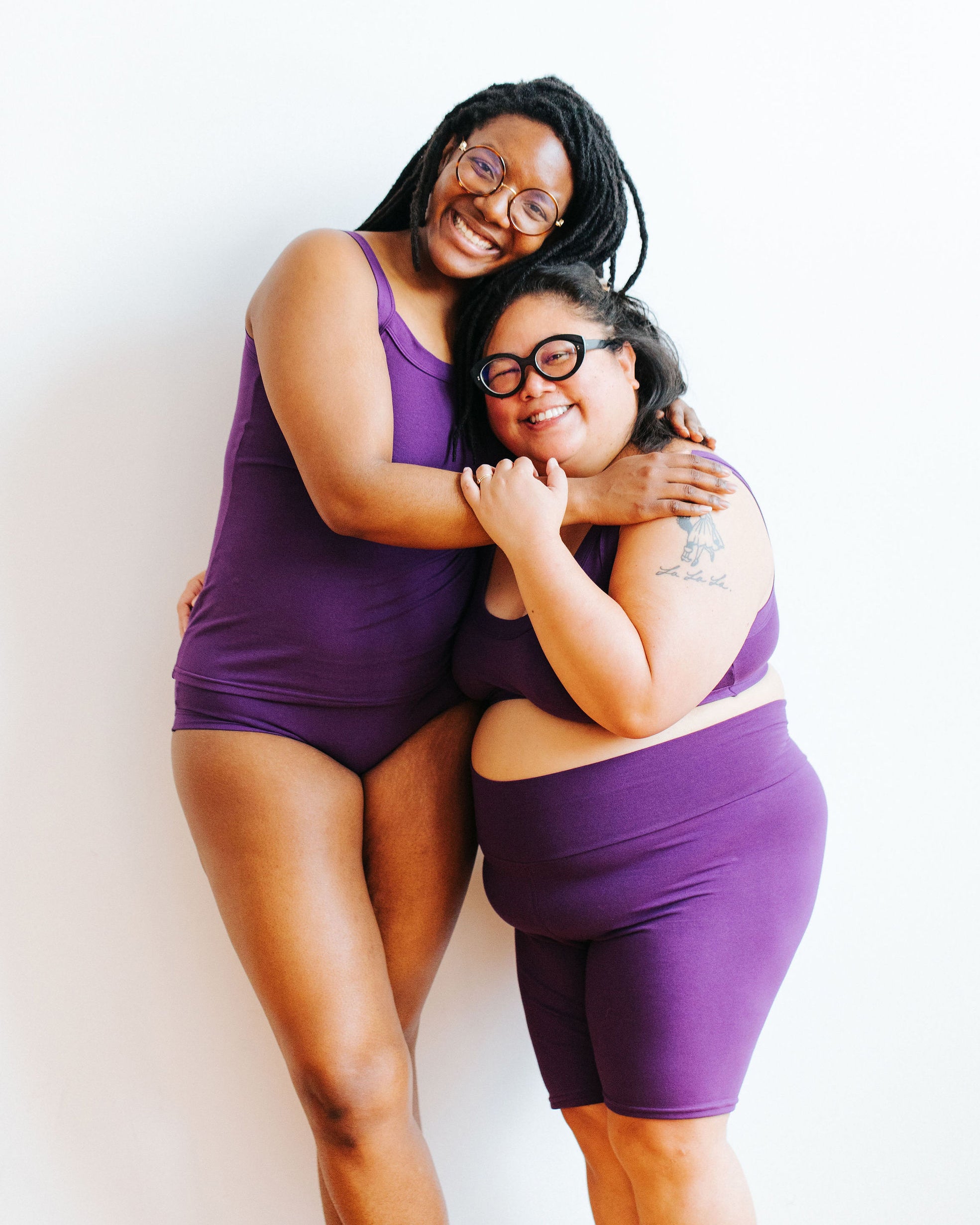 Two models smiling and embracing wearing a Camisole, Hipster style underwear, Bralette, and Bike Shorts in Deep Amethyst.