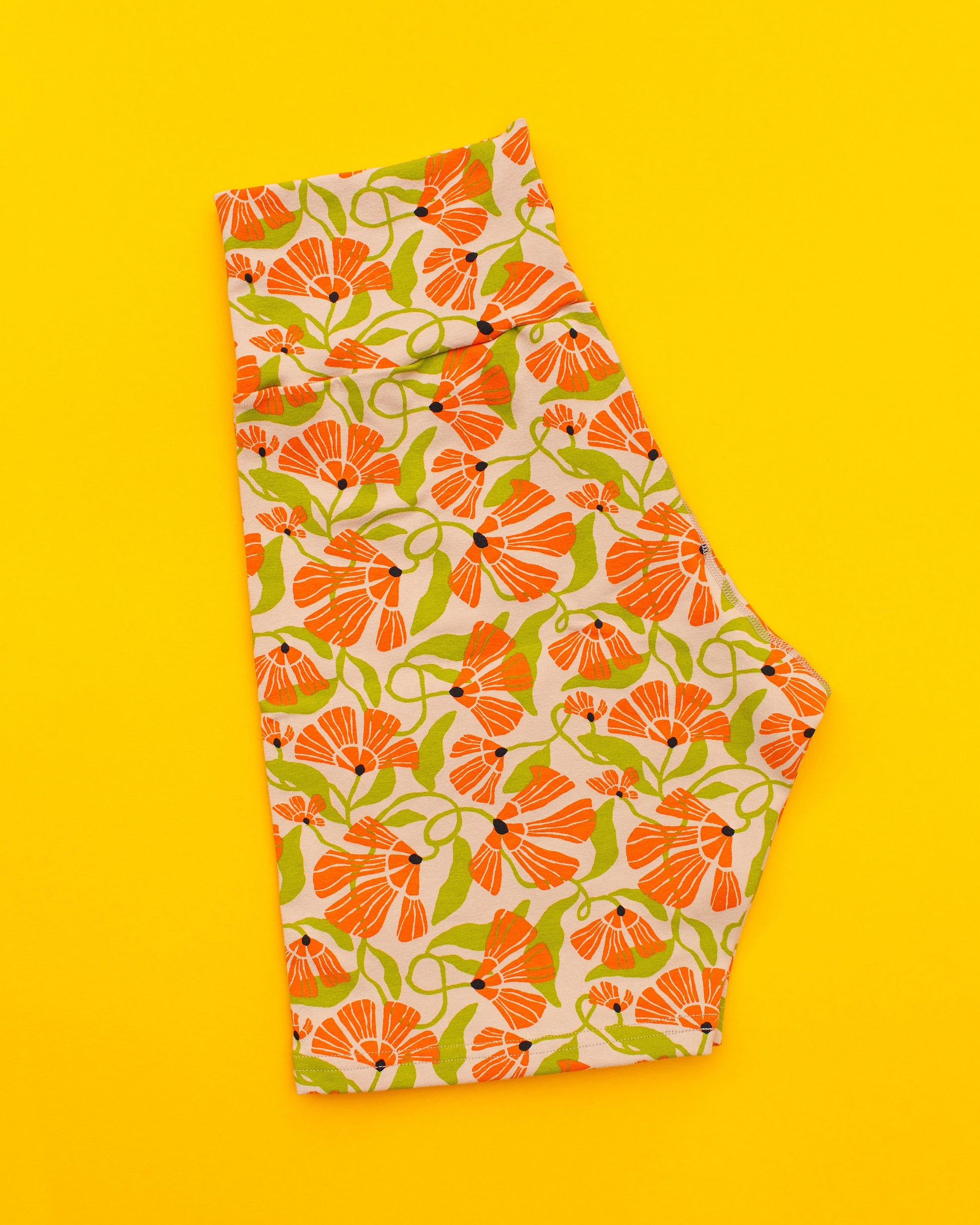 Flat lay of Thunderpants Bike Shorts in Secret Garden - tan background with orange and green flowers.