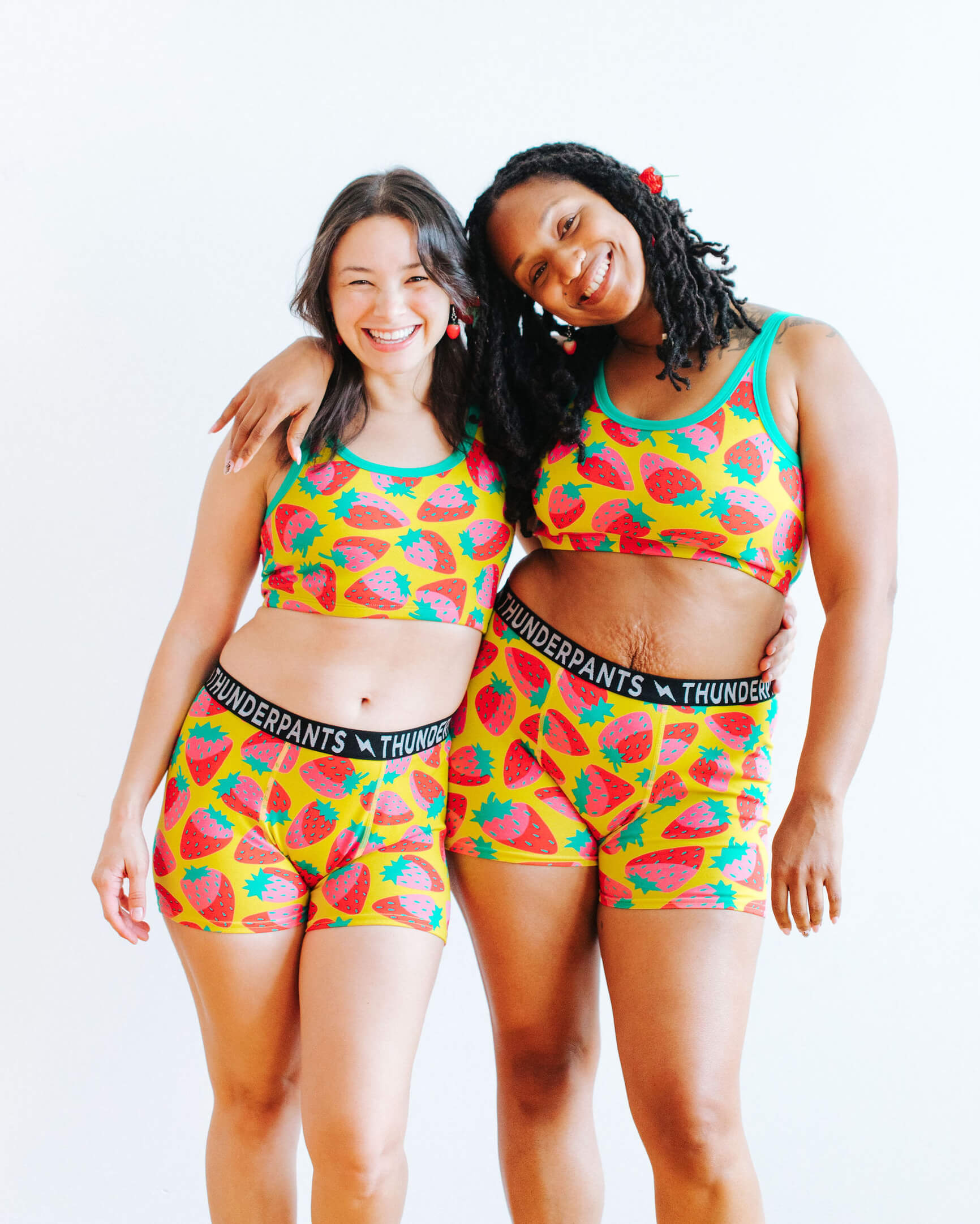 Models wearing Thunderpants Boxer Brief and Longline Bra in a Strawberry print - pink, red, and peacock green on chartreuse.