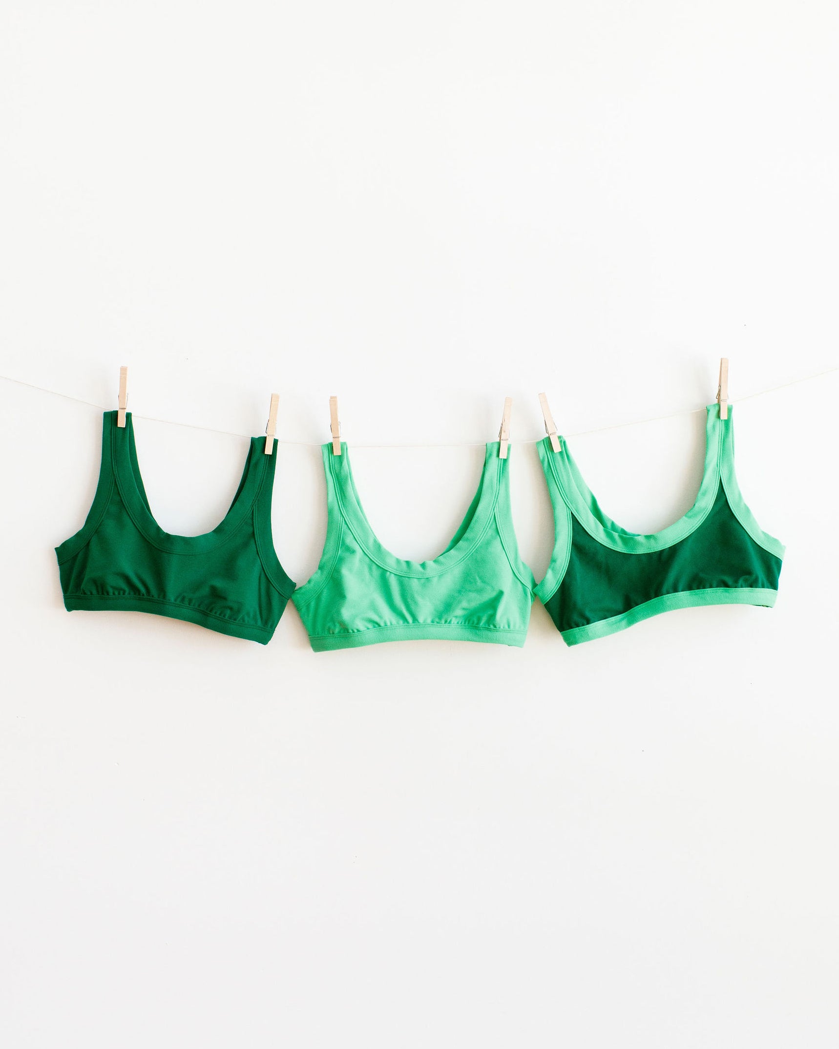 Three pack of different green colored Bralettes hanging on a white wall..