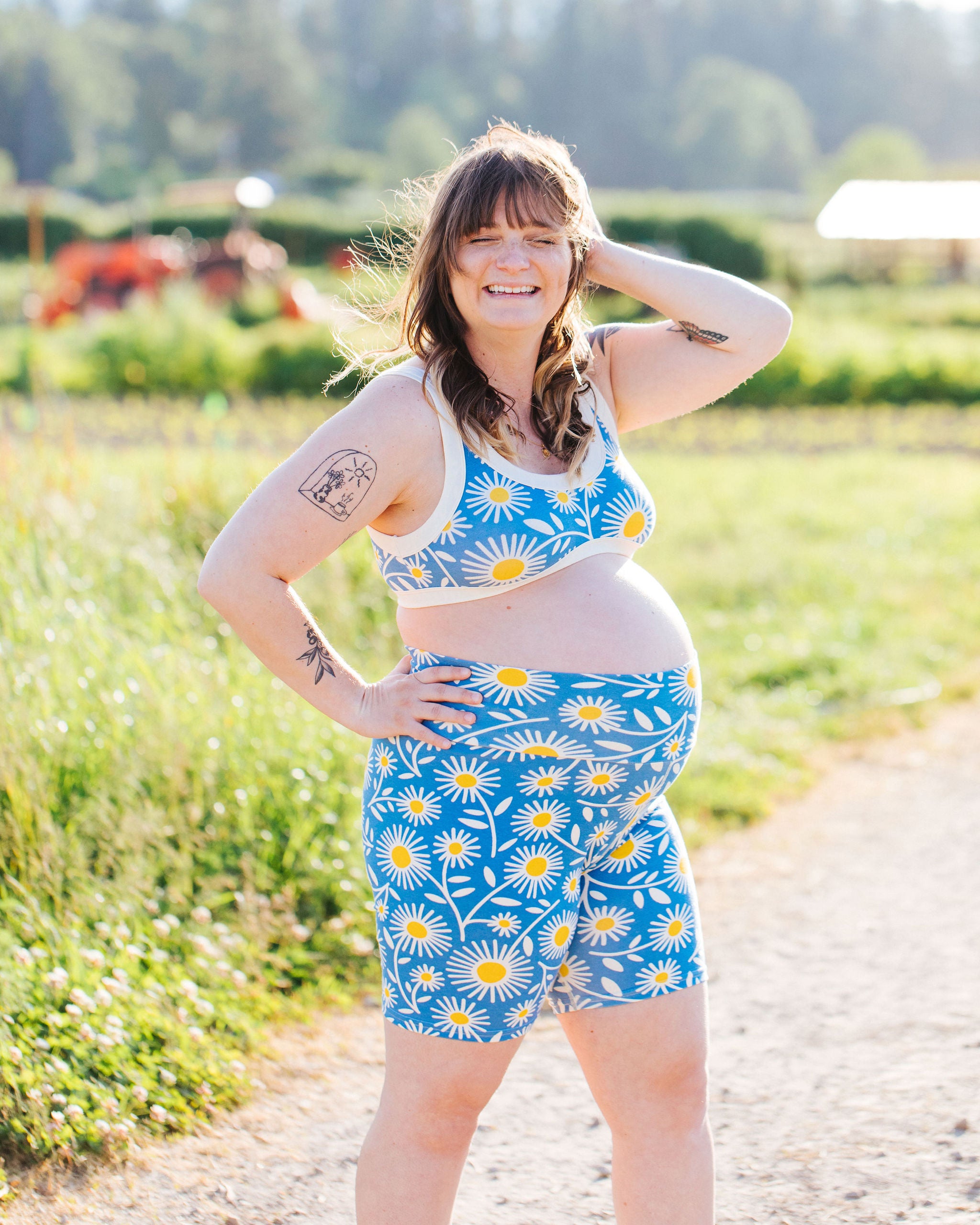 Pregnant model standing in a field wearing Thunderpants Bralette and Bike Shorts in Daisy Days print: blue with white and yellow daisies.