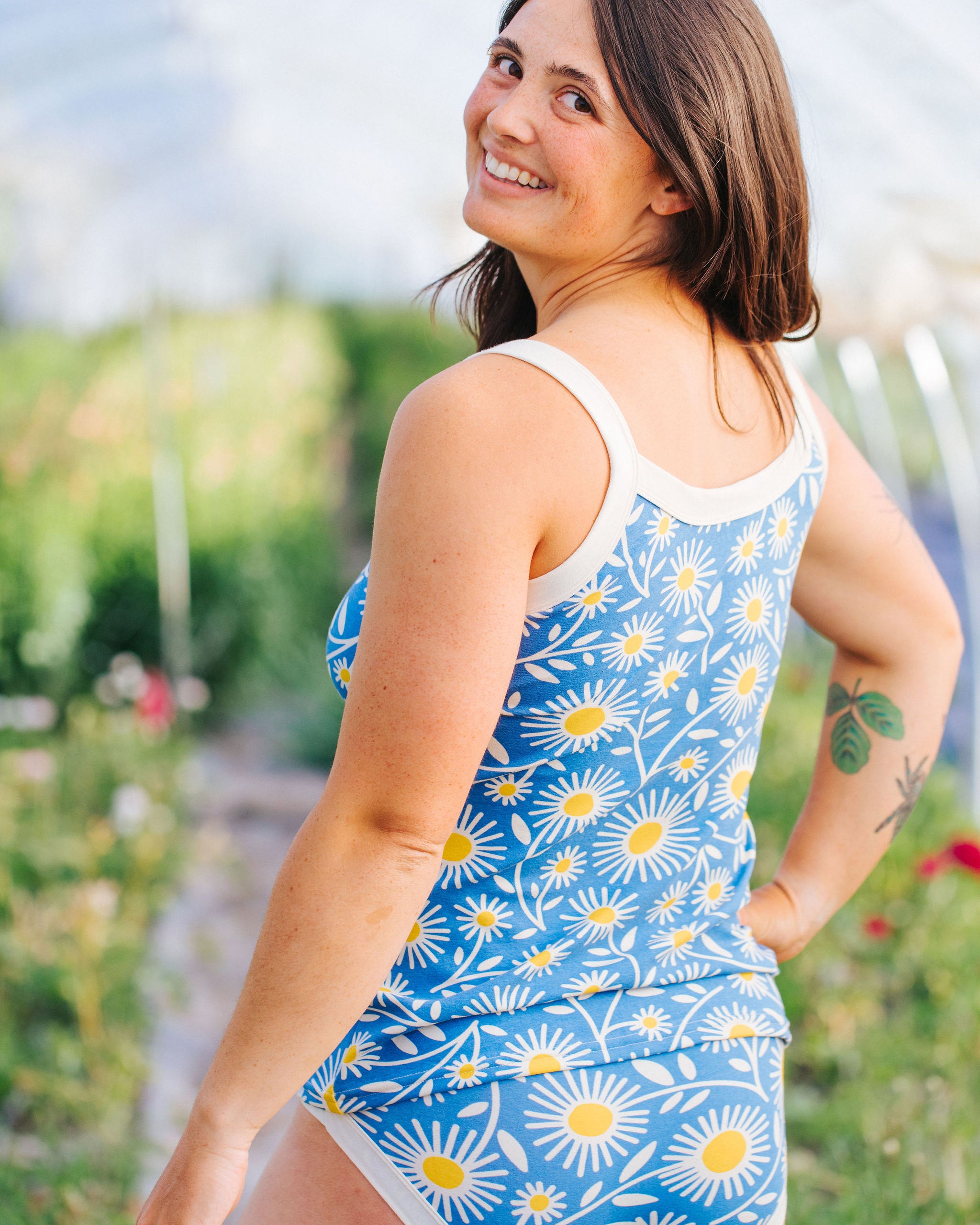 Close up of model smiling in a field wearing Thunderpants Camisole and Hipster style underwear in Daisy Days print: blue with white and yellow daisies.