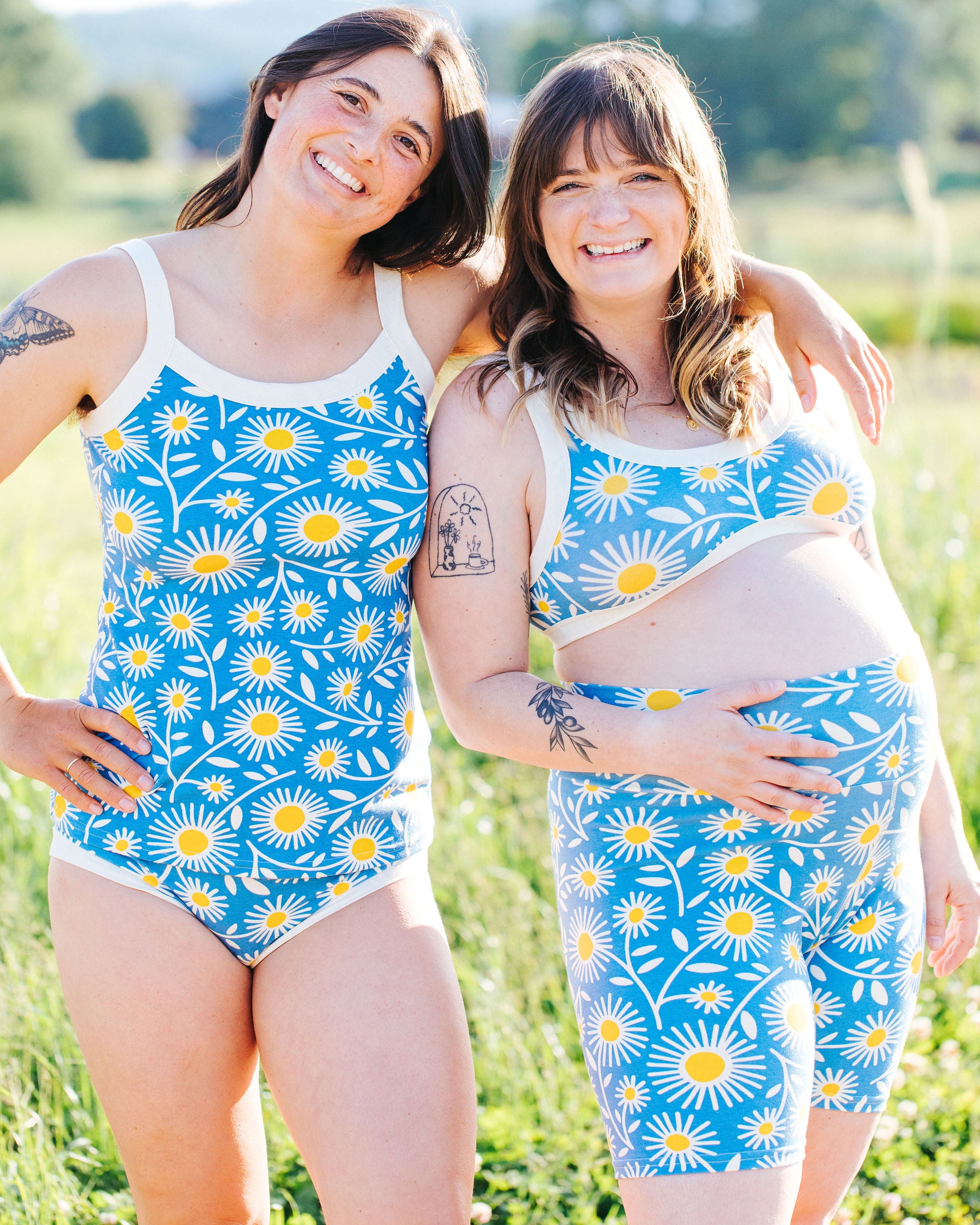 Two model smiling in a field wearing various Thunderpants styles in Daisy Days print: blue with white and yellow daisies.