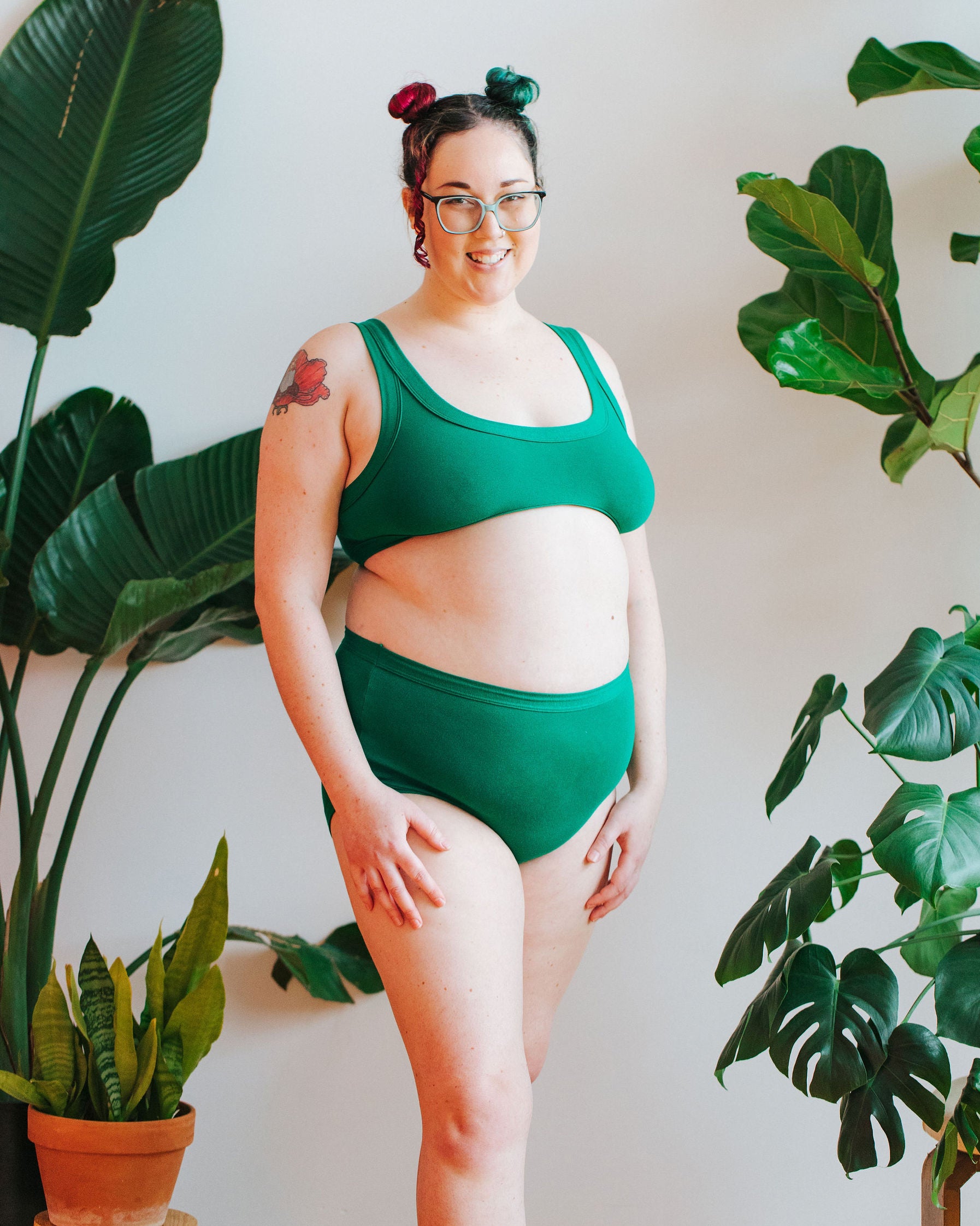 Model smiling in front of a bunch of plants wearing a Bralette and Original style underwear in Emerald Green.