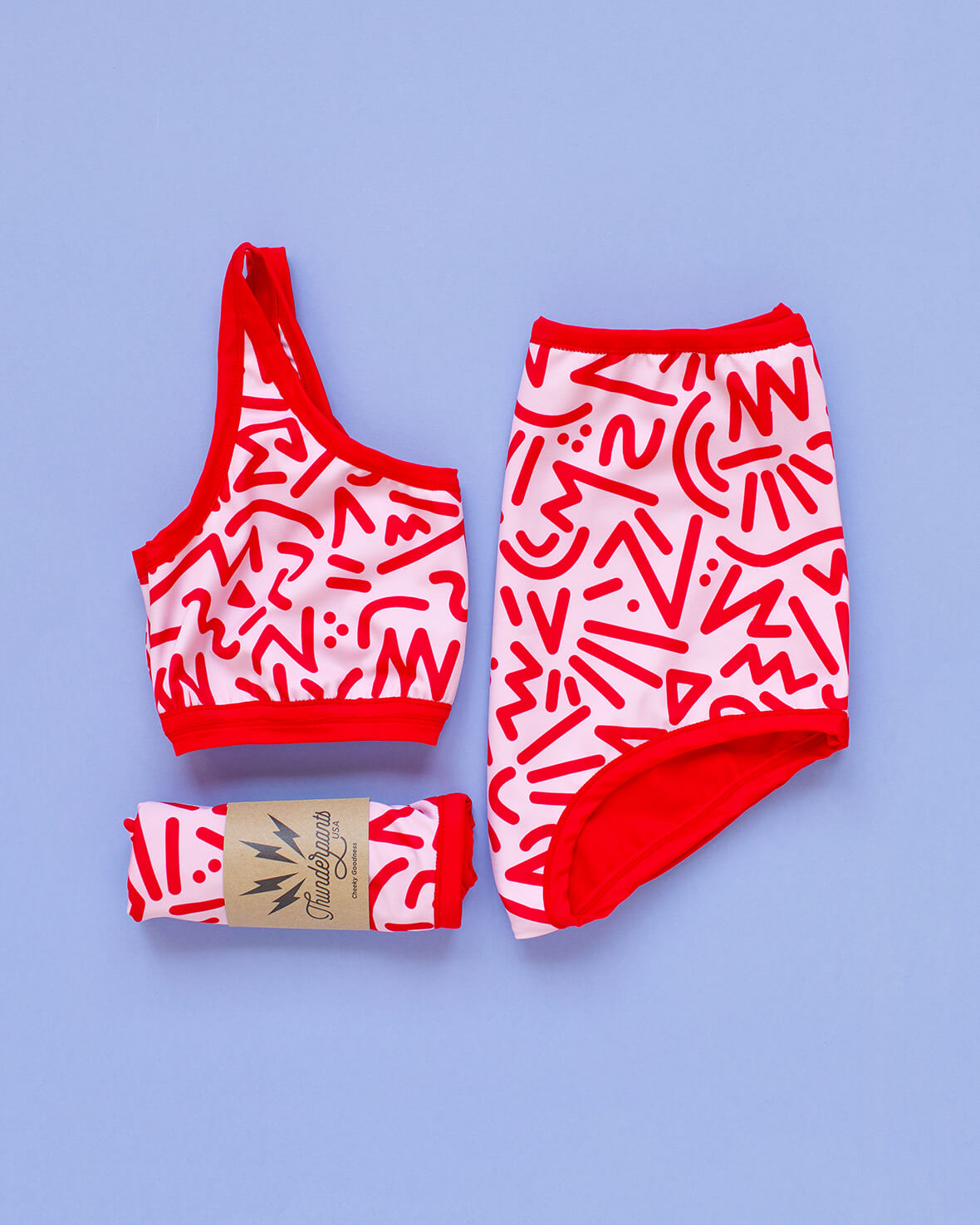 Flat lay of Thunderpants Sky Rise style Swim Bottoms and Swim Top in Energy Vibe print: light pink with dark pink designs.