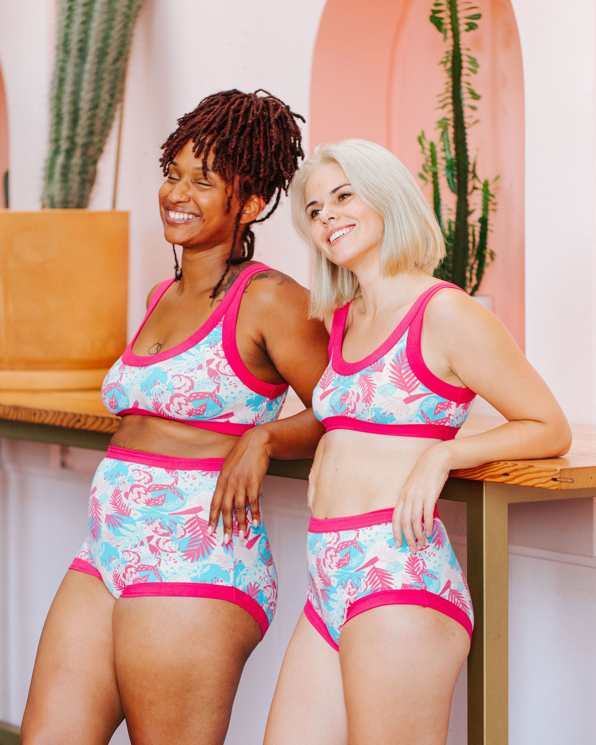 Two models laughing while wearing sets in Thunderpants Bralettes and underwear in Finding Flamingos - pink and blue Miami-inspired print.
