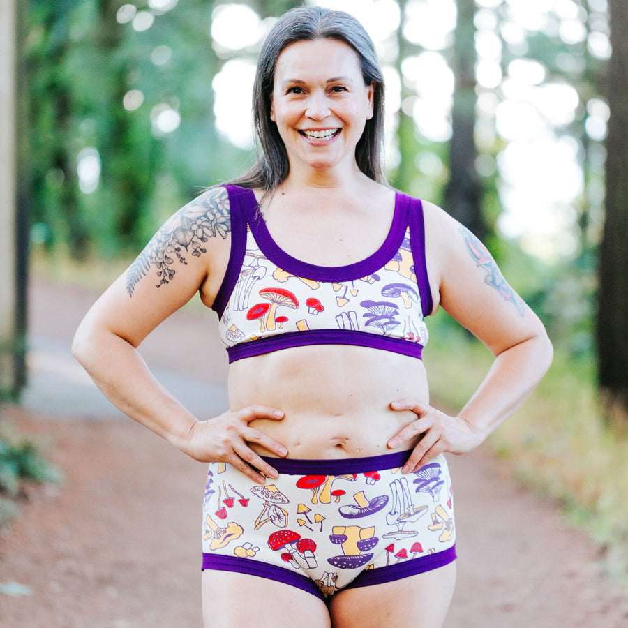 Close up of model wearing Bike Shorts in Mushroom Magic print: different mushrooms in red, yellow, and purple colors.