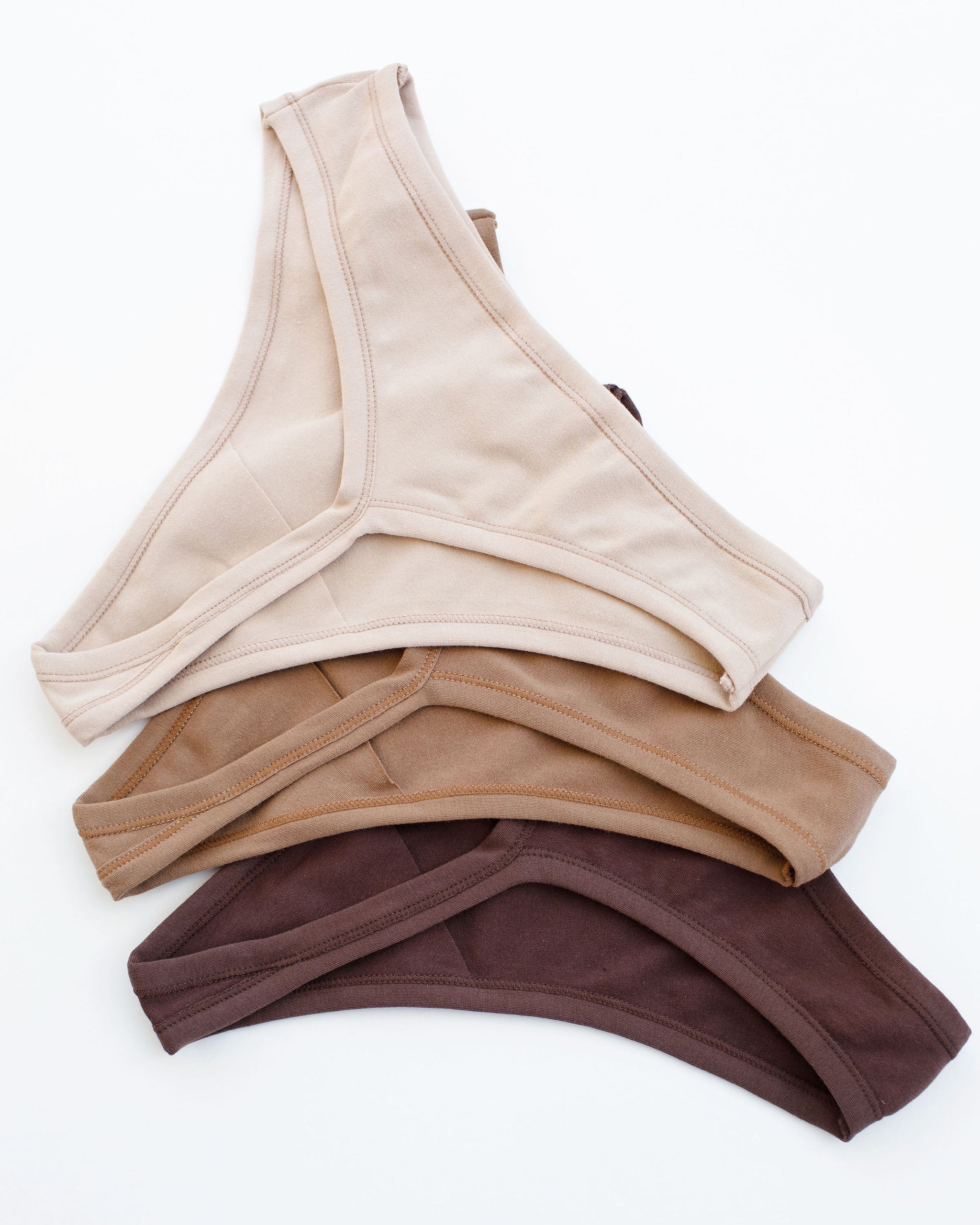 Flay lay of Thunderpants Thong style underwear in Pine Nut (a tan), Hazelnut (a light brown), and Chestnut (a dark brown).