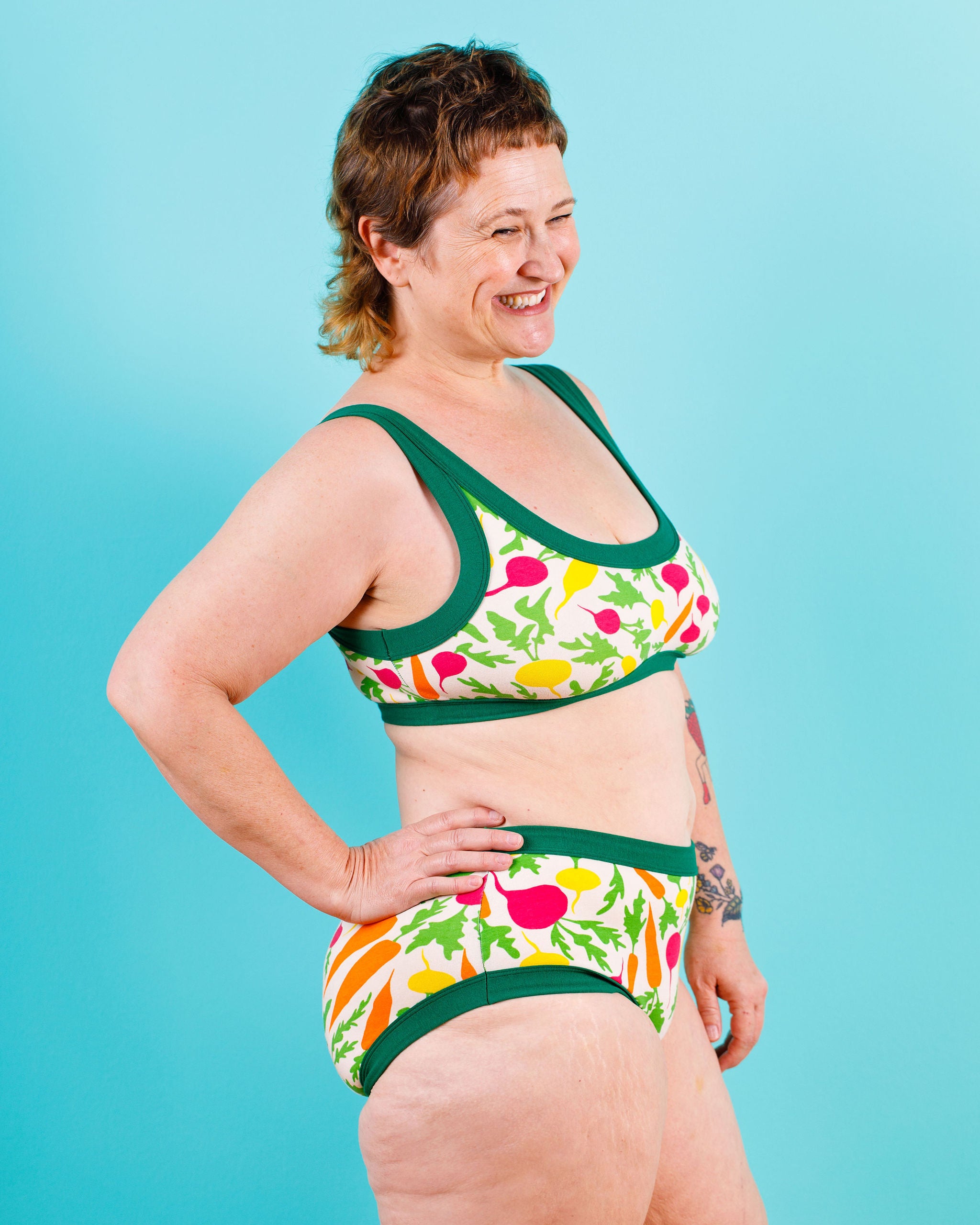 Model smiling wearing  Thunderants Hipster style underwear and matching Bralette in Root Veggies print - yellow, orange, pink, and green vegetables.