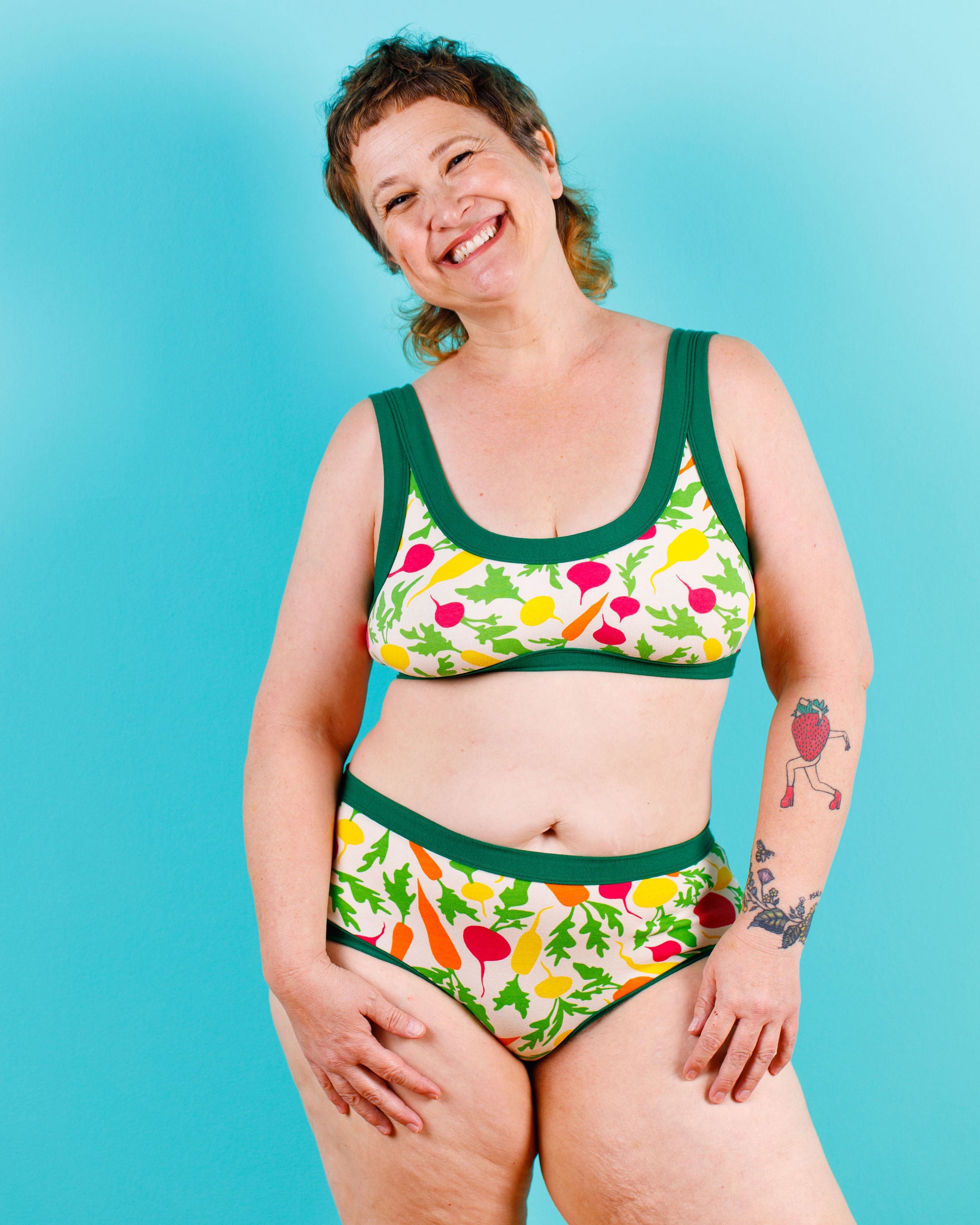 Model smiling wearing  Thunderants Hipster style underwear and matching Bralette in Root Veggies print - yellow, orange, pink, and green vegetables.