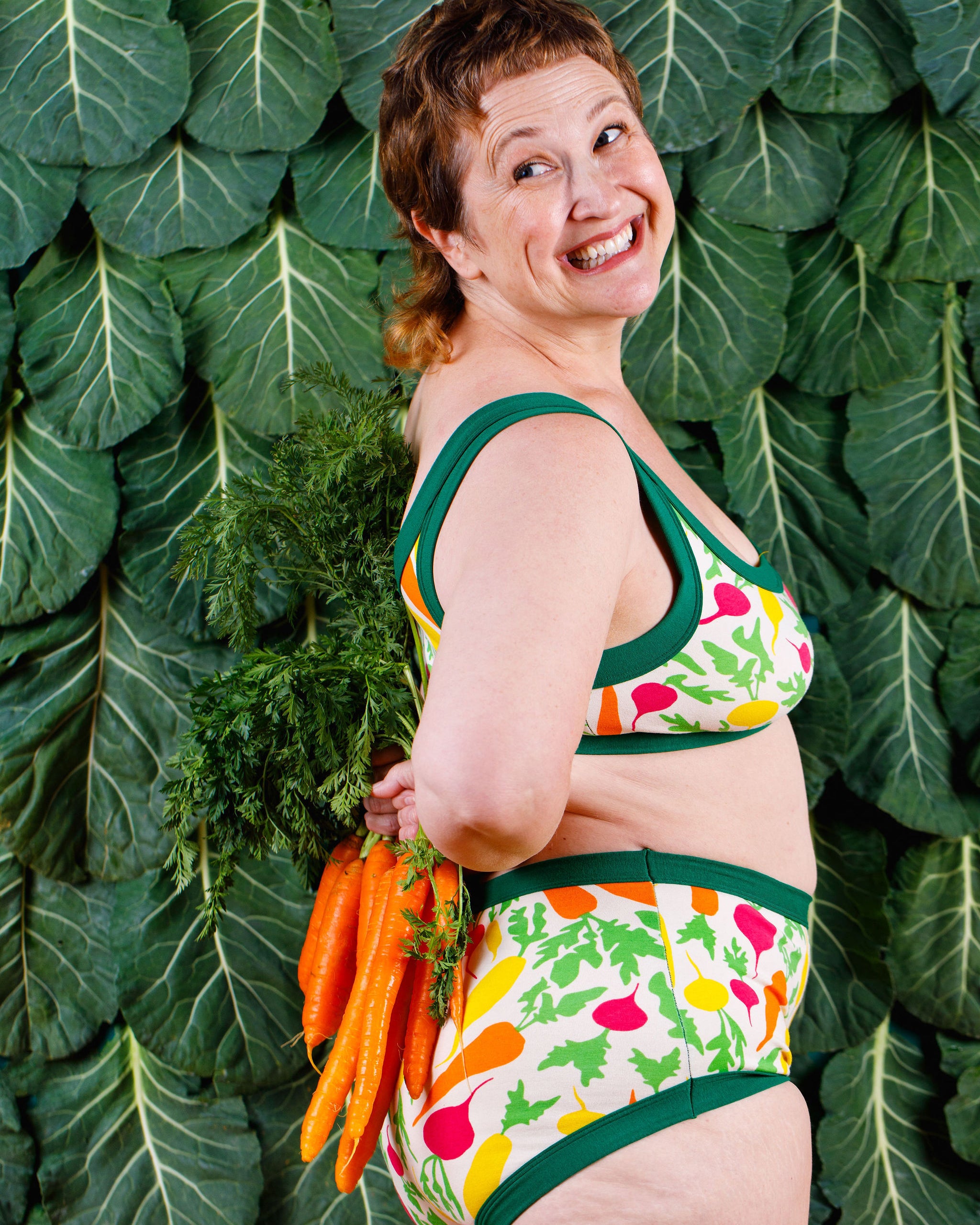 Model smiling wearing Thunderants Original style underwear and matching Bralette in Root Veggies print - yellow, orange, pink, and green vegetables.