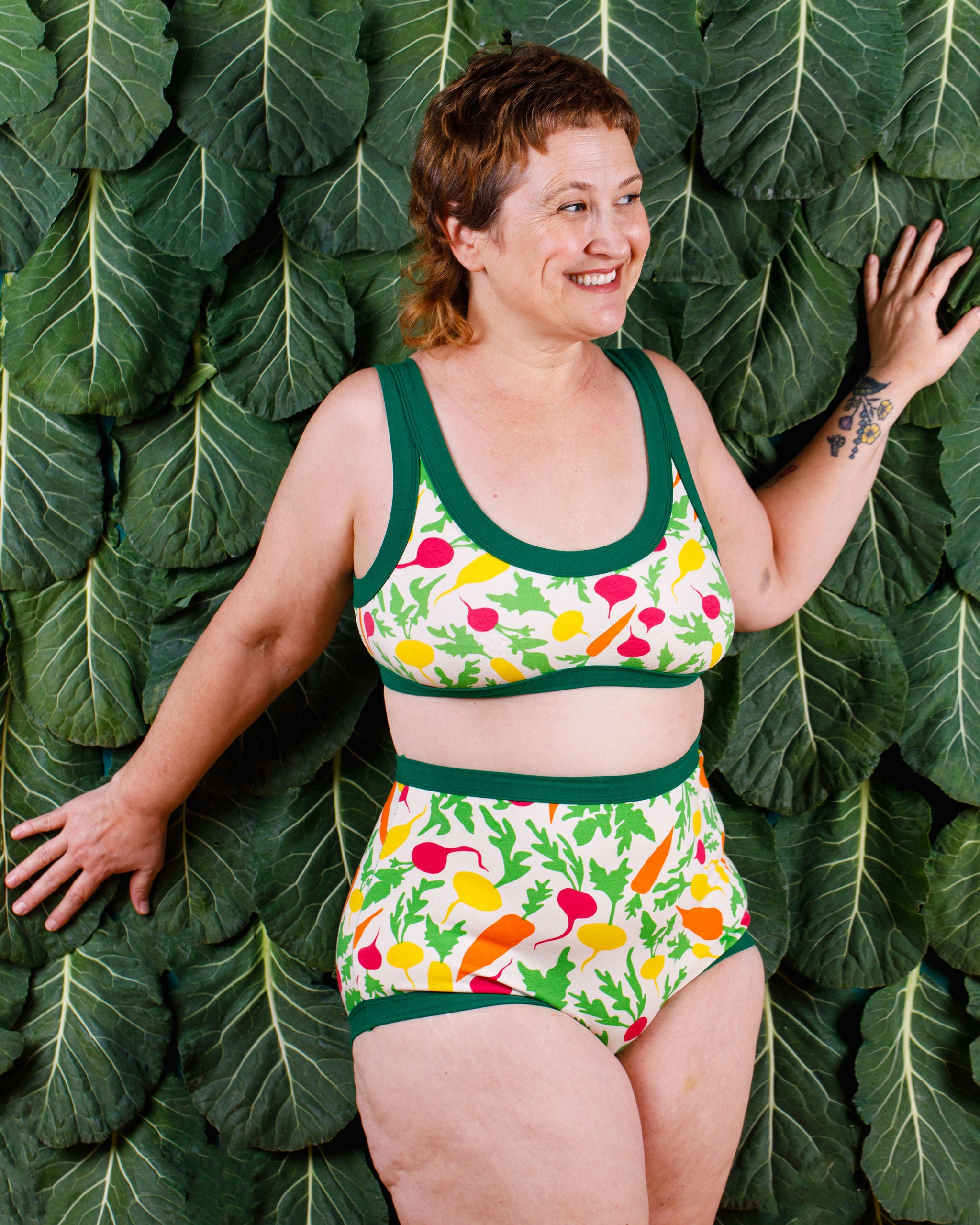 Model smiling wearing Thunderants Sky Rise style underwear and matching Bralette in Root Veggies print - yellow, orange, pink, and green vegetables.