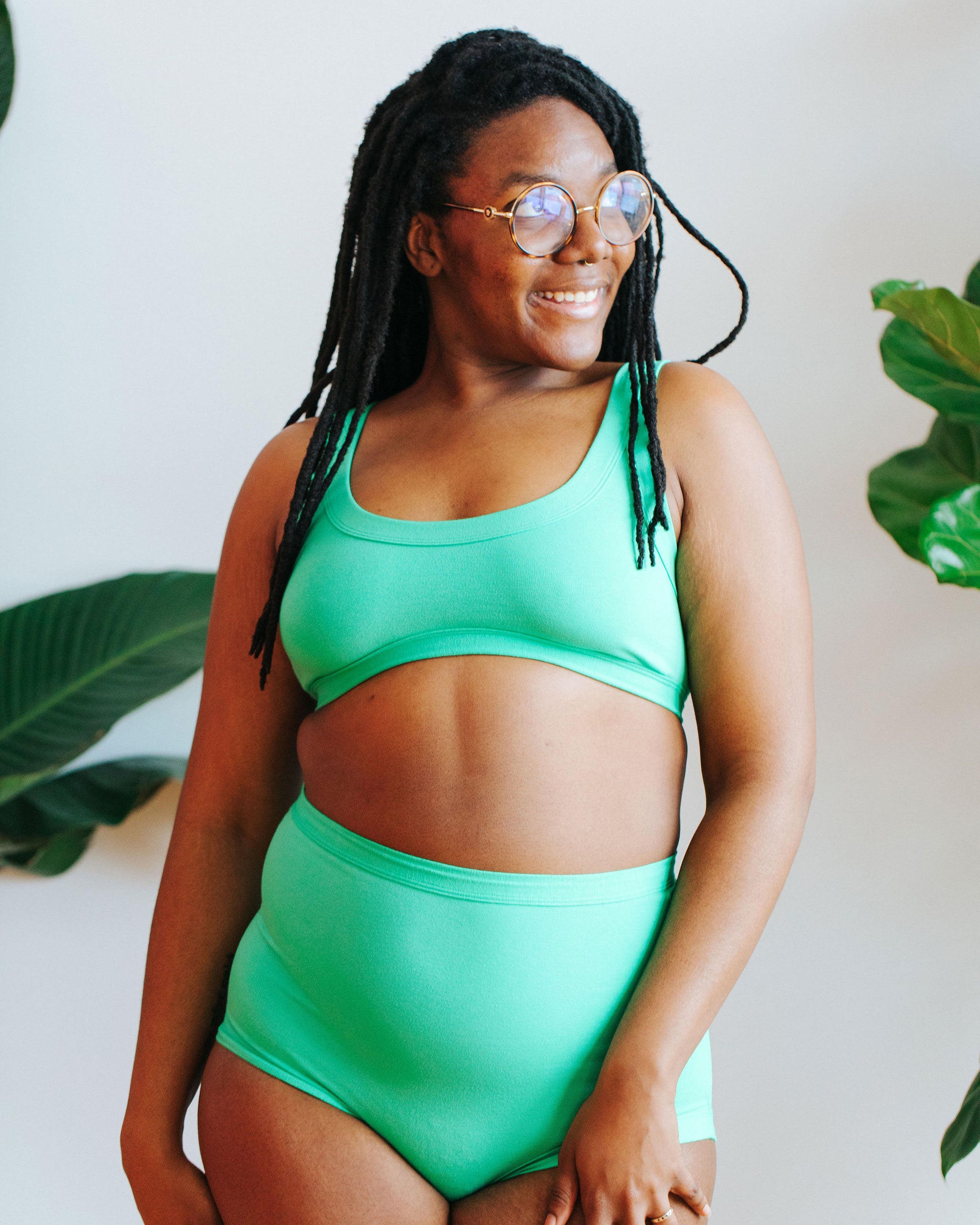 Close up of model in front of plants wearing a Bralette and Sky Rise style underwear in the light green color Sour Apple.