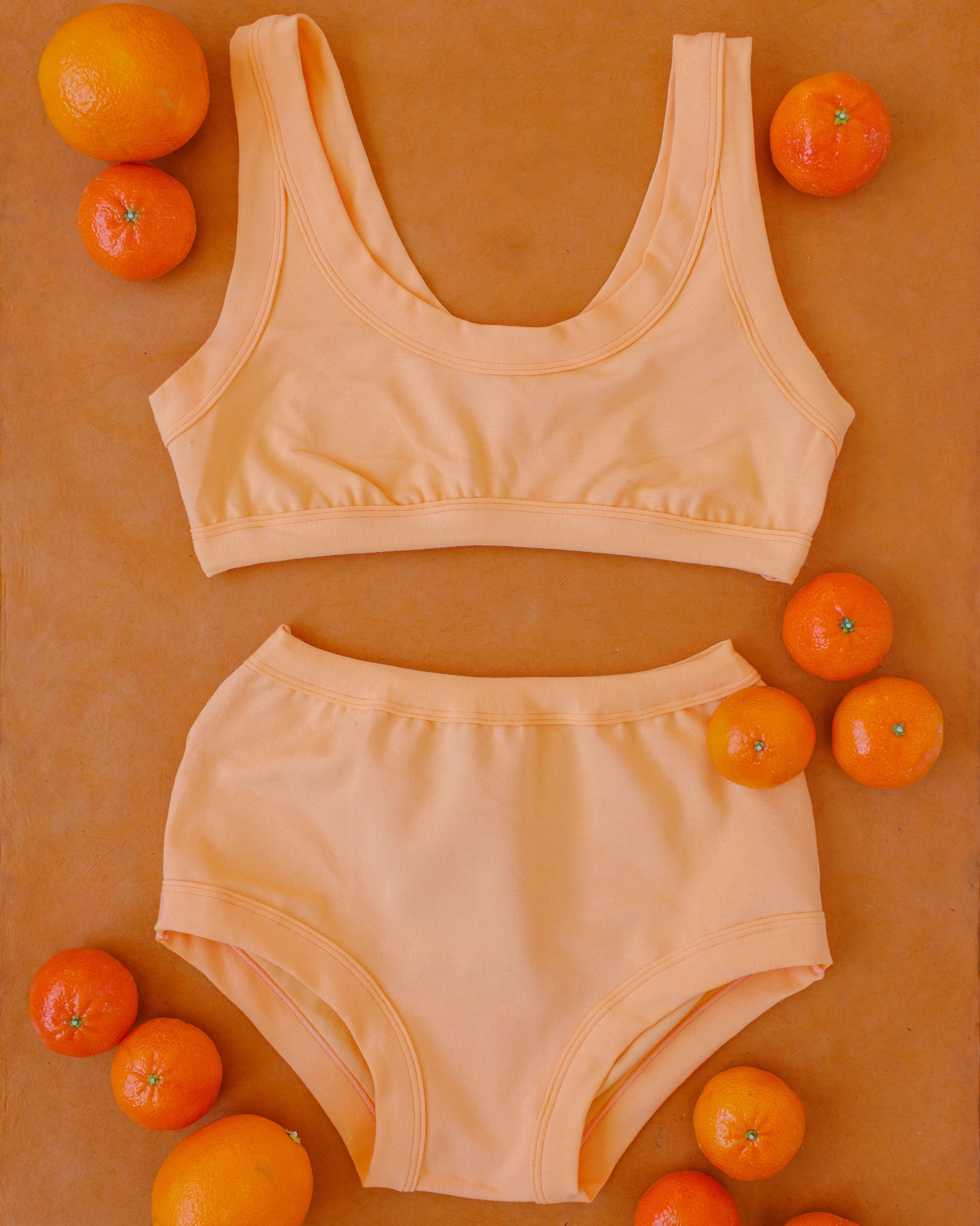 Flat lay of an Orange Sherbet set of Original style underwear and Bralette with oranges surrounding it.