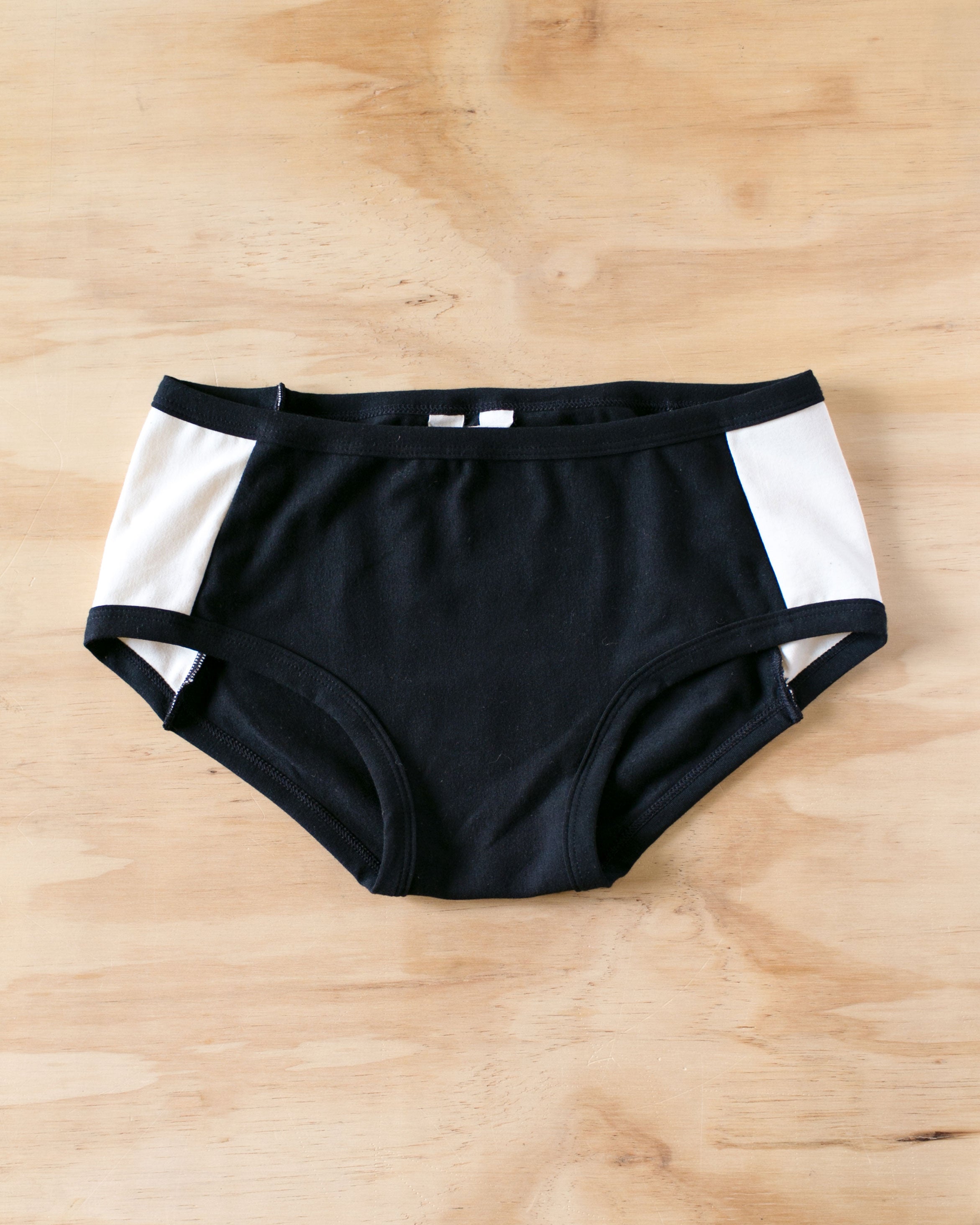Flat lay on wood of our Cookies and Cream Panel Pants in the Hipster style: black panel in the center and vanilla panels on both sides with black binding.