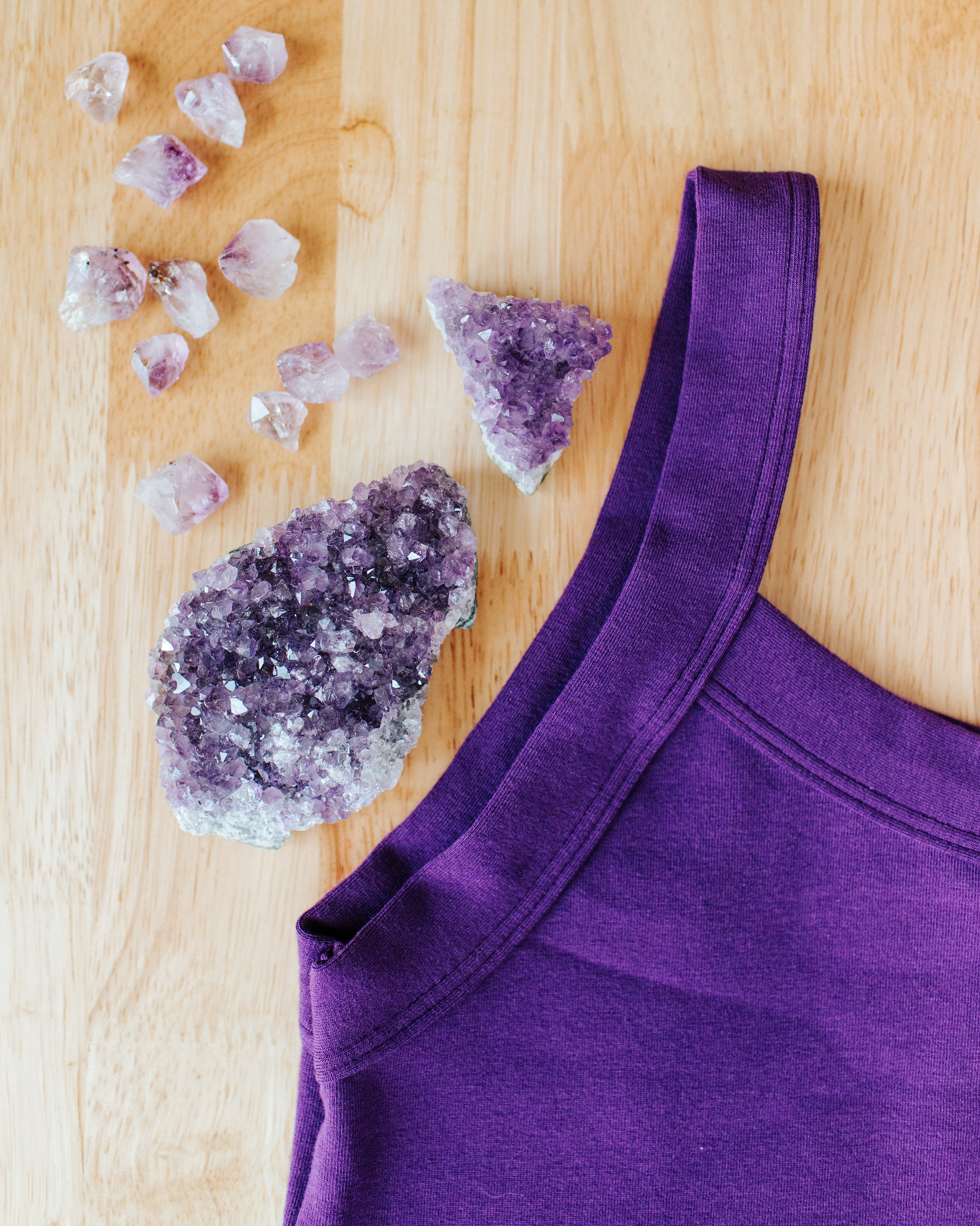 Close up flat lay of purple Deep Amethyst Camisole on a wood surface with large and small amethyst stones.
