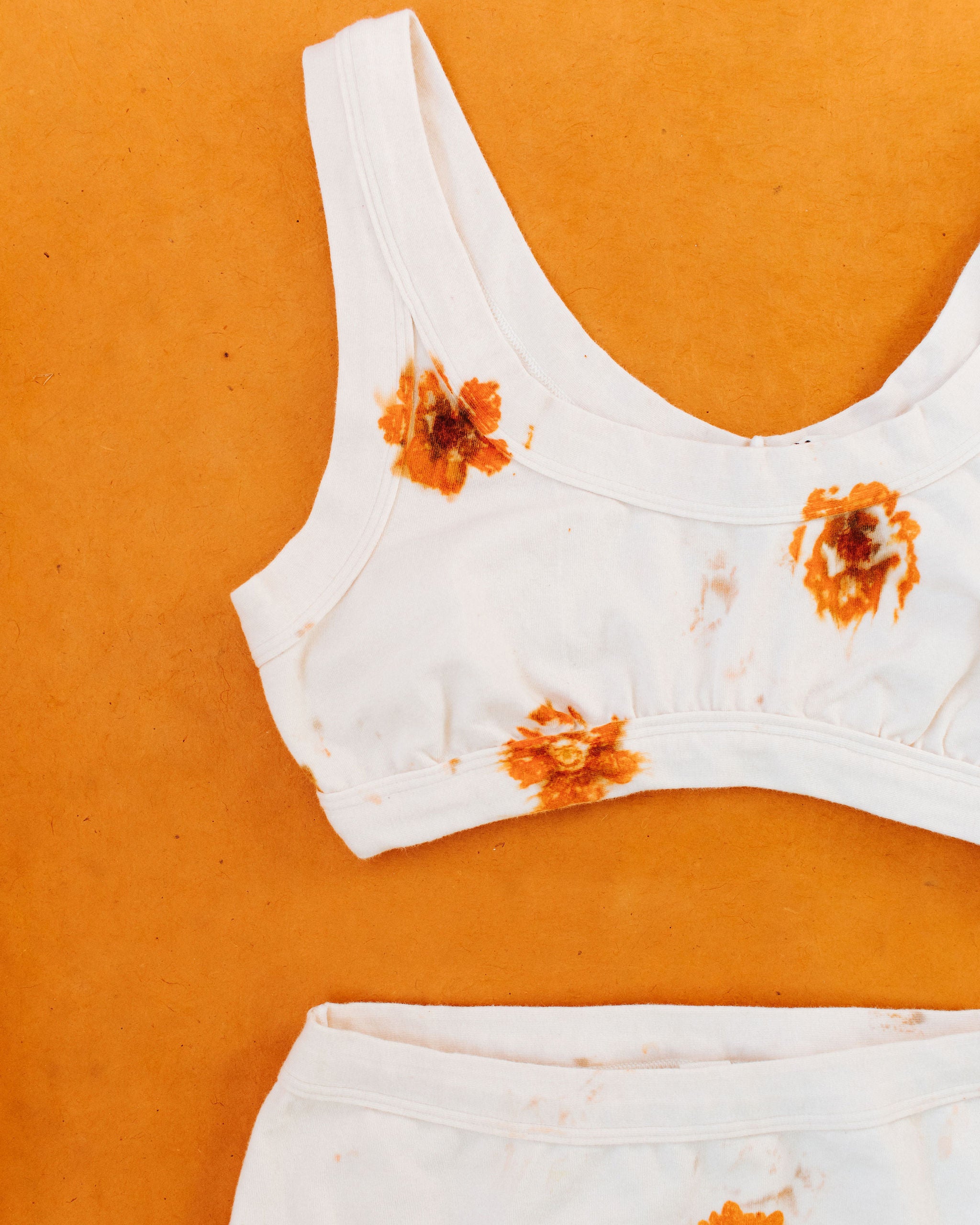 Close up flat lay on an orange surface of Thunderpants Bralette in the Limited Edition Flower Press Botanical Dye - flowers pressed on our fabric to create prints.