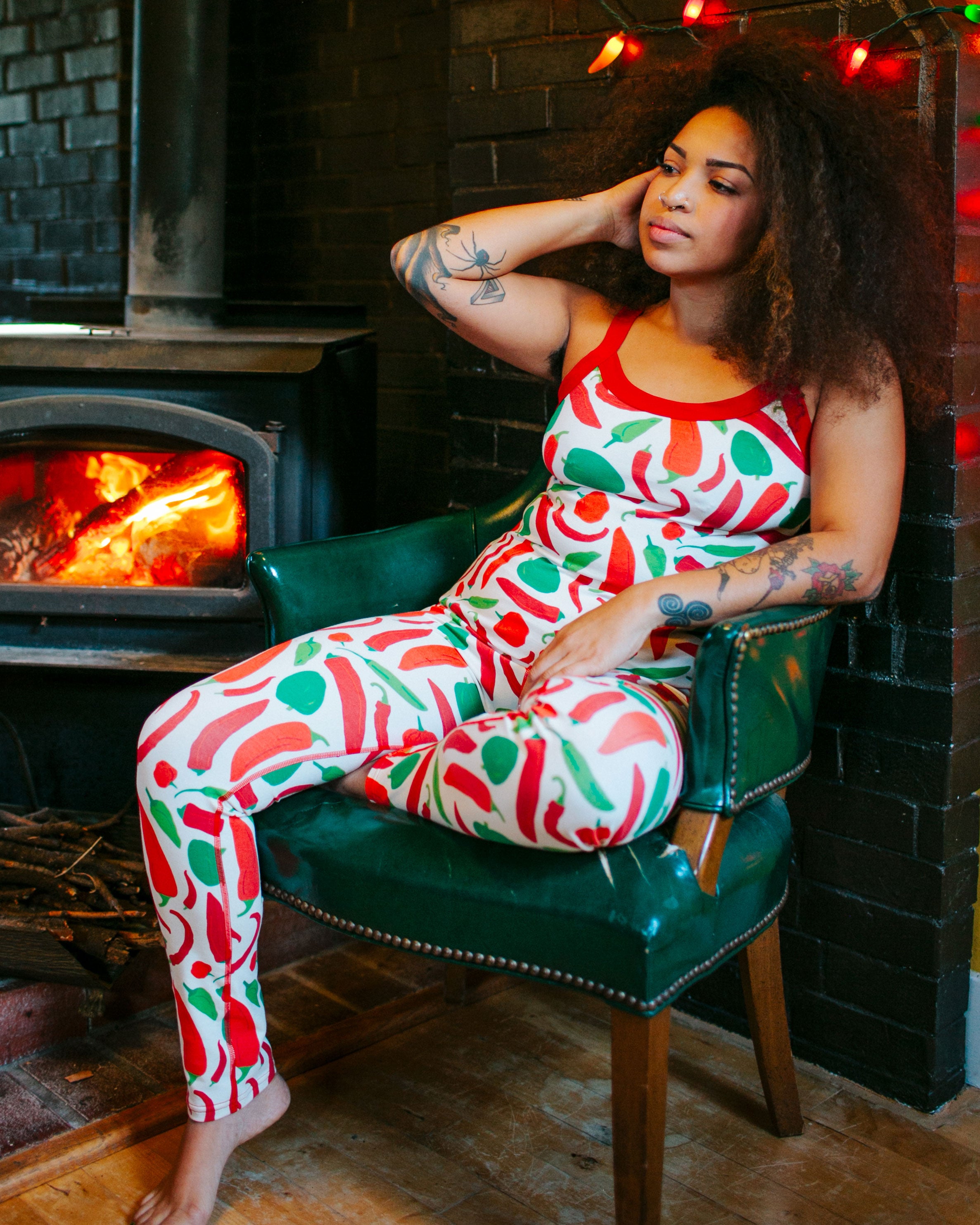Model sitting by the fire inside wearing Thunderpants organic cotton Camisole and Leggings in our Hot Pants print: various green, orange, and red peppers printed on Vanilla with red binding.