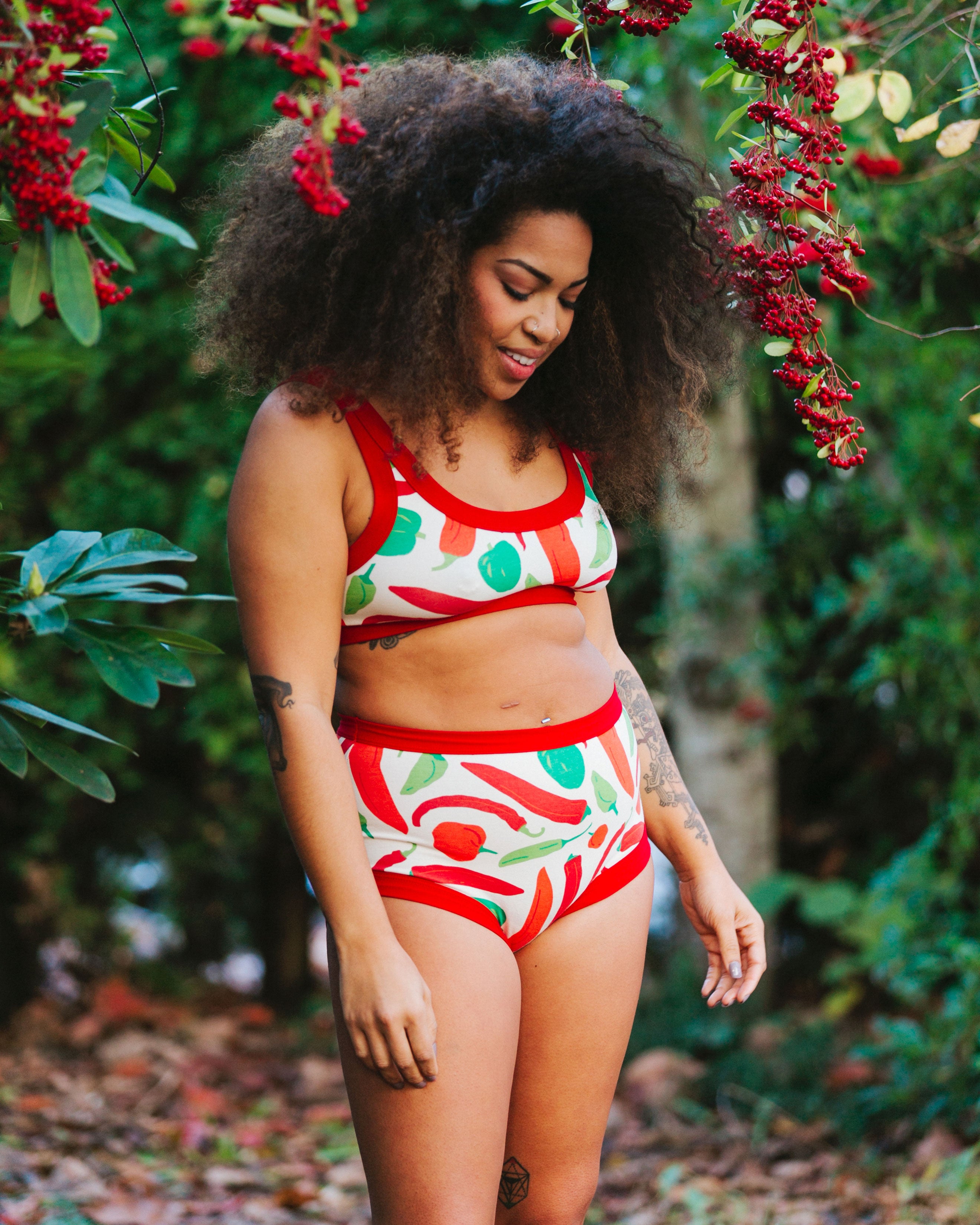 Model standing outside wearing Thunderpants organic cotton Original style underwear and Bralette in our Hot Pants print: various green, orange, and red peppers printed on Vanilla with red binding.