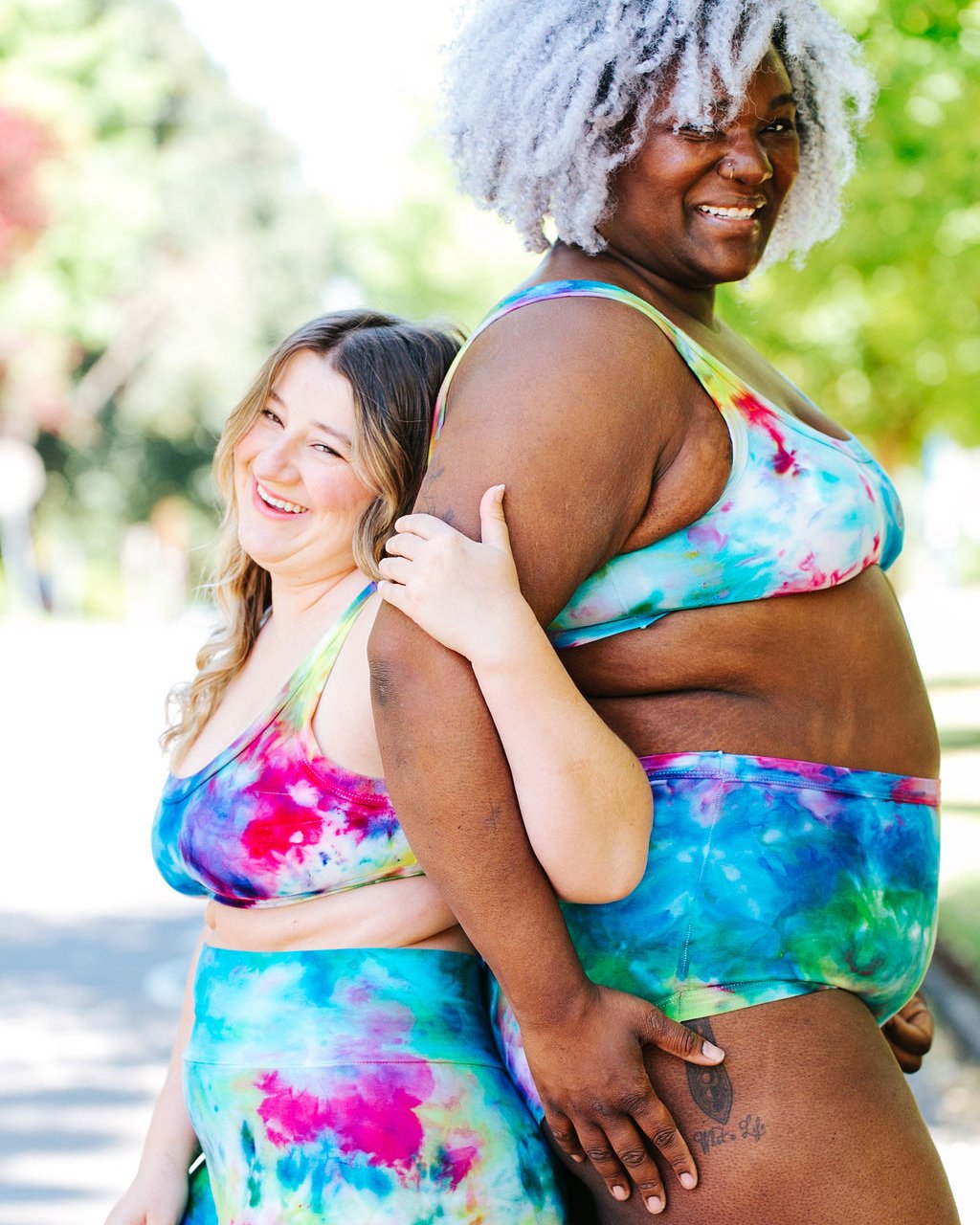 Two models standing back to back wearing Thunderpants Organic Cotton Bralettes and Original style underwear in hand dye Ice Dye multicolored tie-dye.