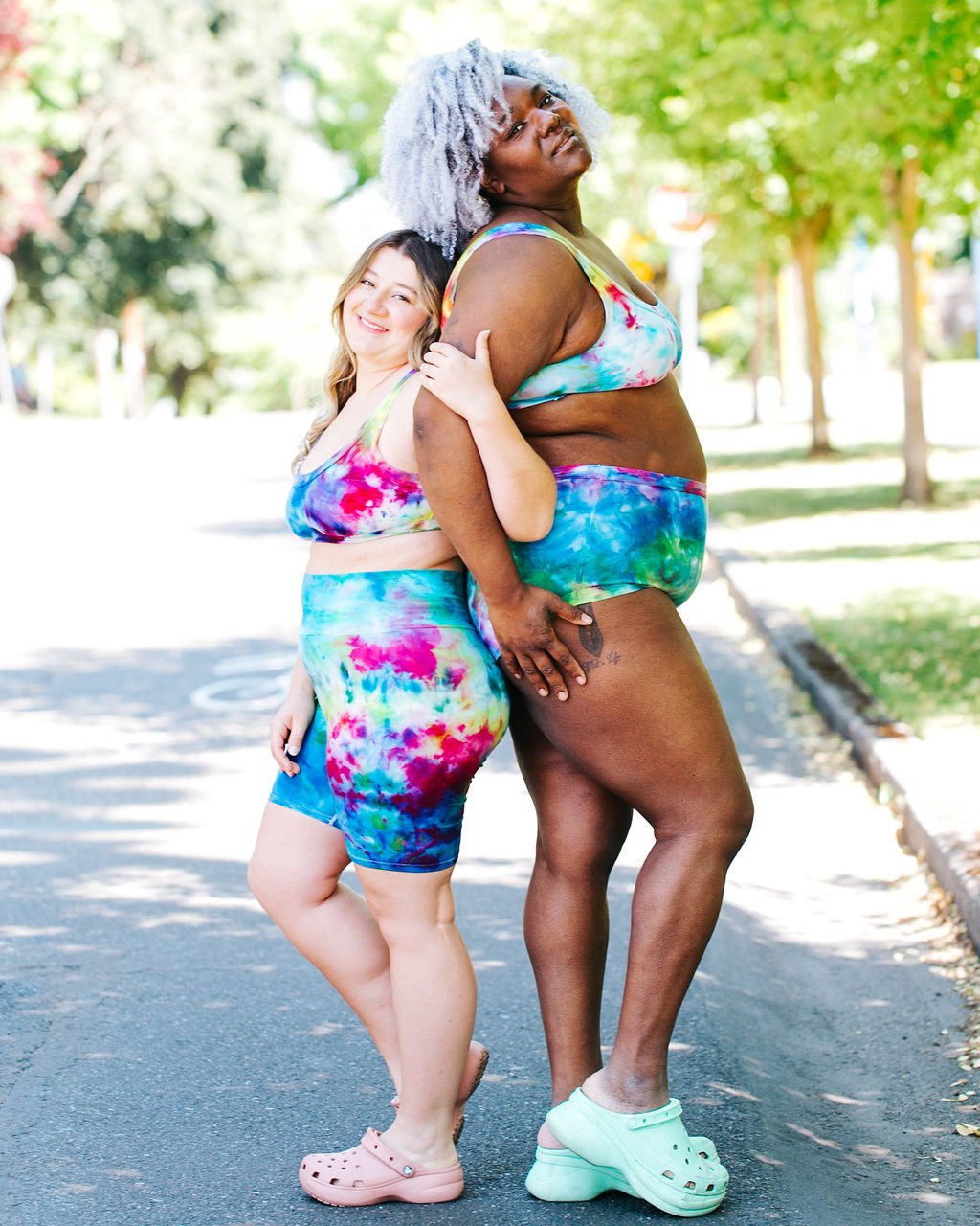 Two models back to back wearing Thunderpants organic cotton Bralettes, Original style underwear, and Bike Shorts in hand dyed Ice Dye multi-colored tie-die.