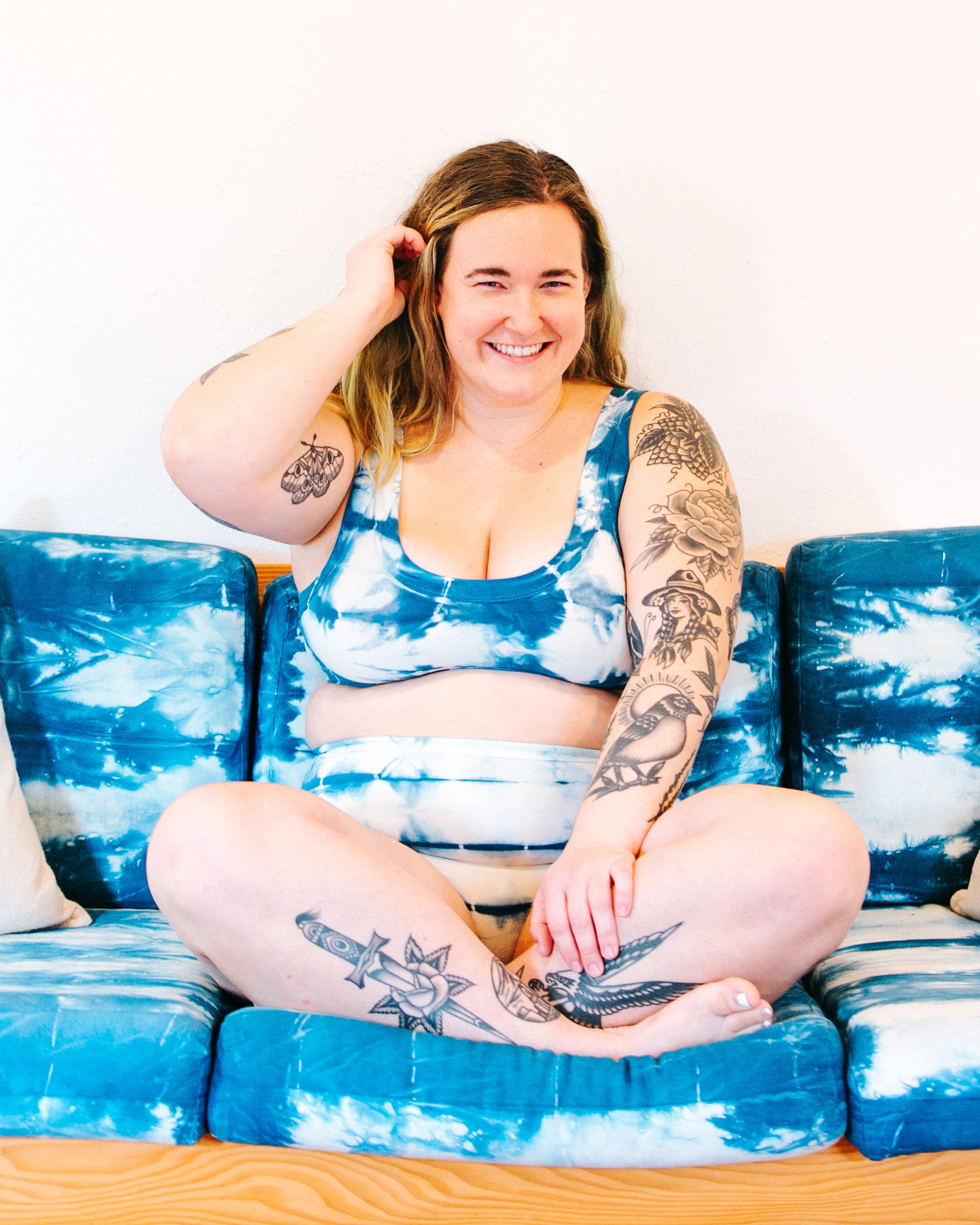 Photo from the front of Thunderpants Organic Cotton Bralette and Sky Rise style underwear in shibori hand dyed Indigo on a model sitting on a shibori indigo dyed couch.