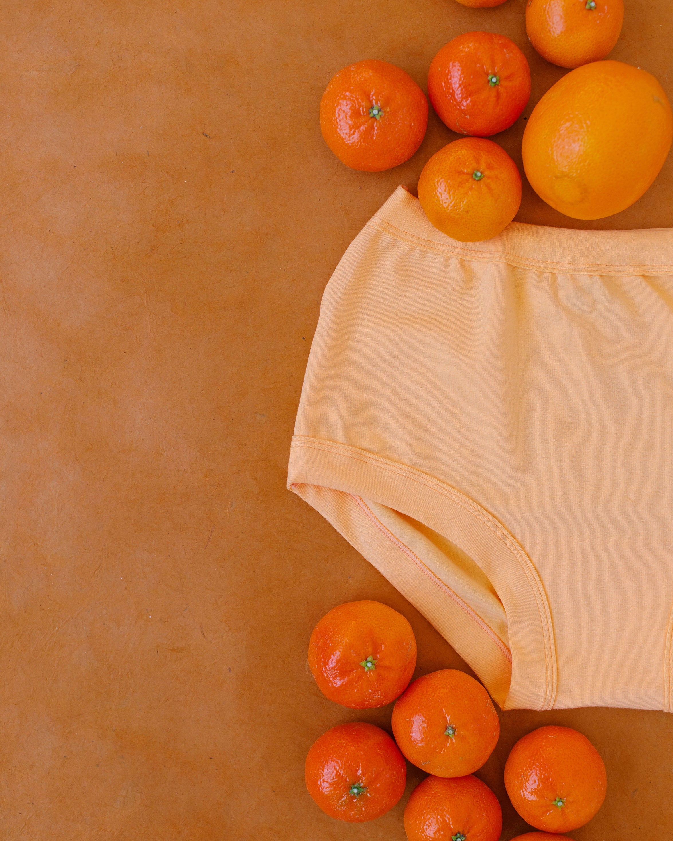 Close up flat lay of Orange Sherbet Original style underwear on an orange surface with oranges around it.
