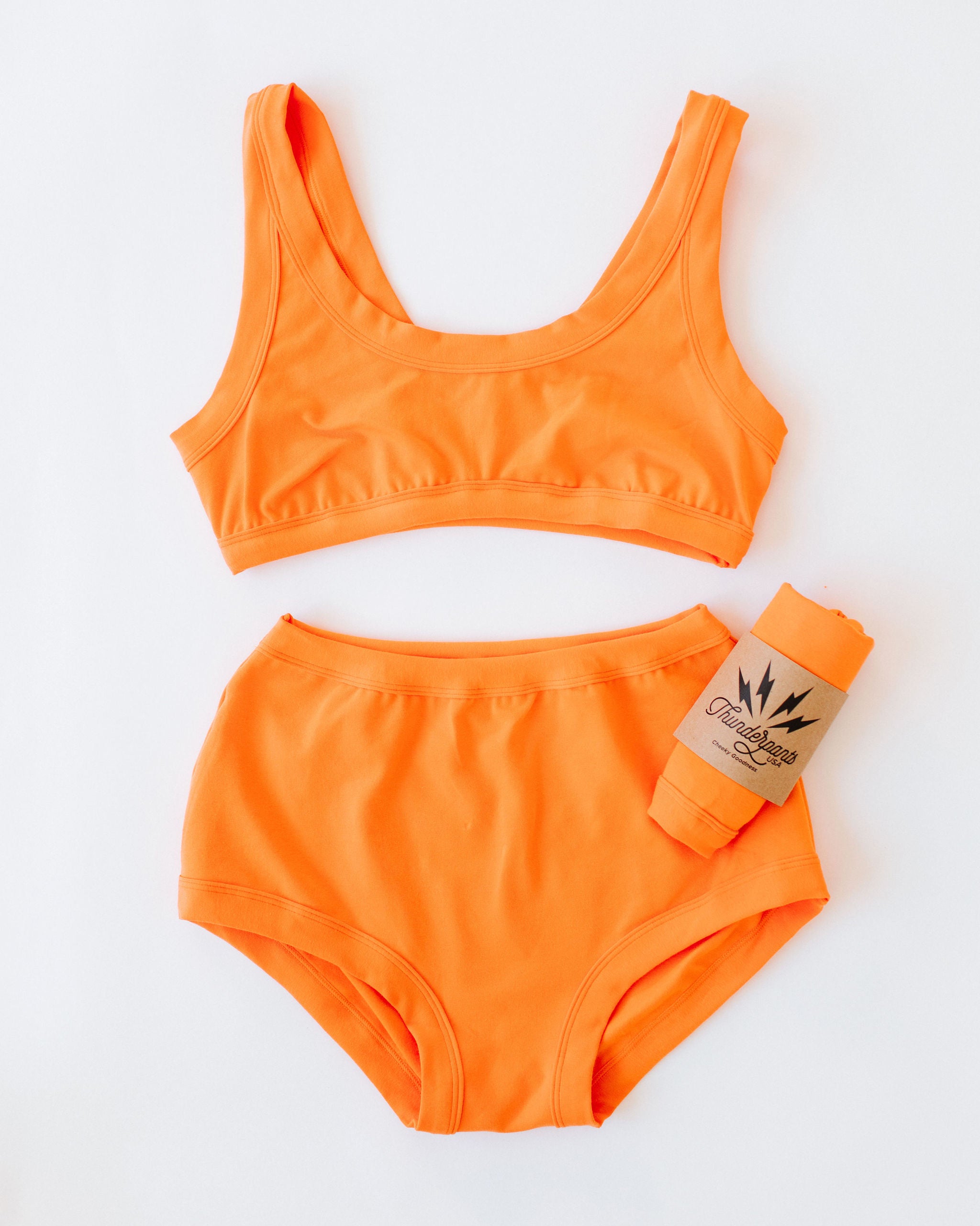 Flat lay of Thunderpants Original style underwear and Bralette in Oregon Sunstone orange color. 