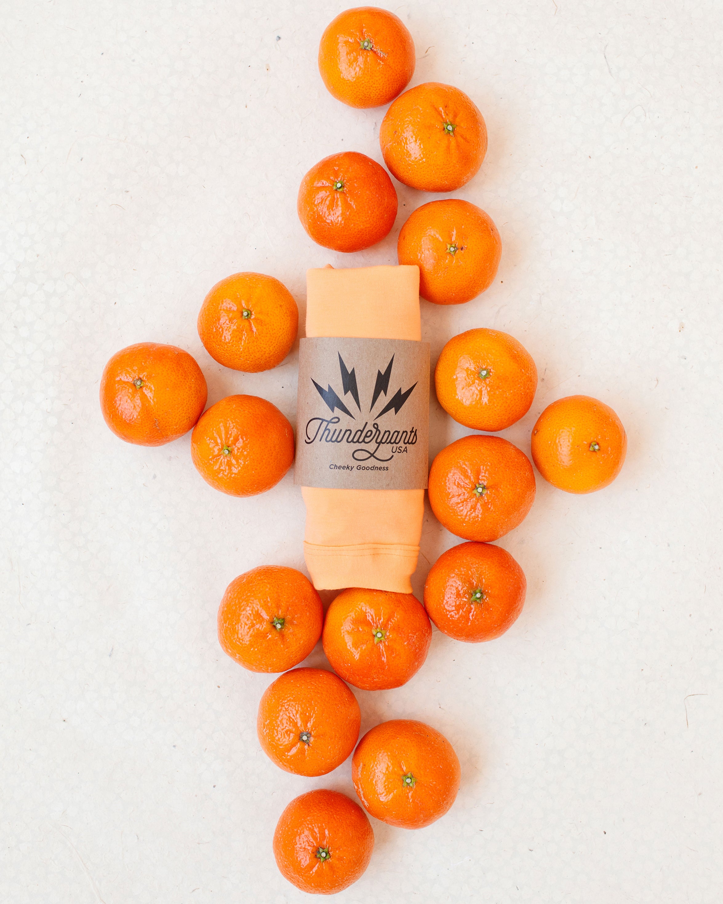 Flat lay of packaged Orange Sherbet underwear on a white patterned surface with oranges surrounding it.