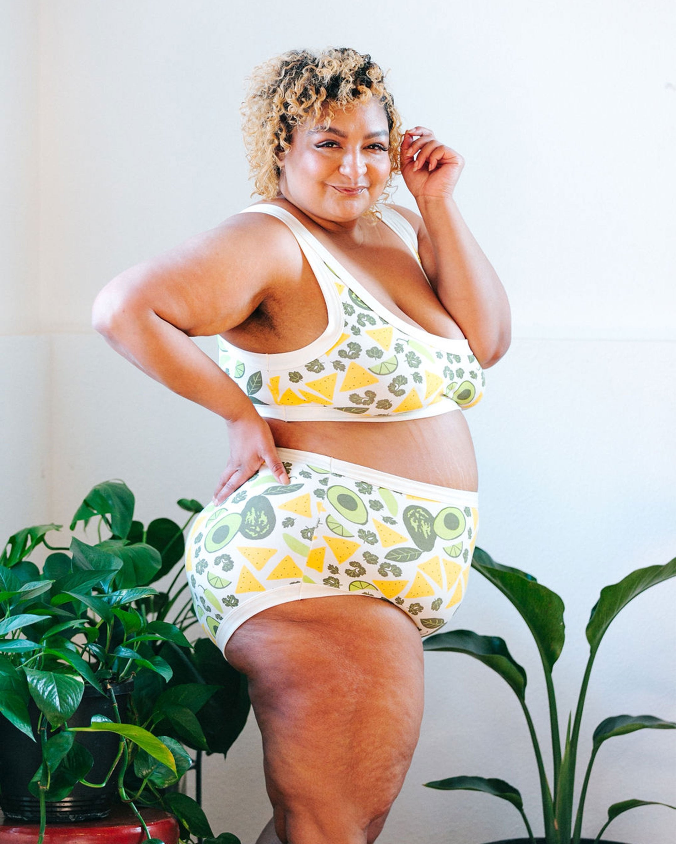 Plus-sized model wearing Thunderpants organic cotton Original style underwear and Bralette in our Party Guac print: a deconstructed guacamole (avocado, cilantro, pepper, lime, and tortilla chip) print with plants around her.