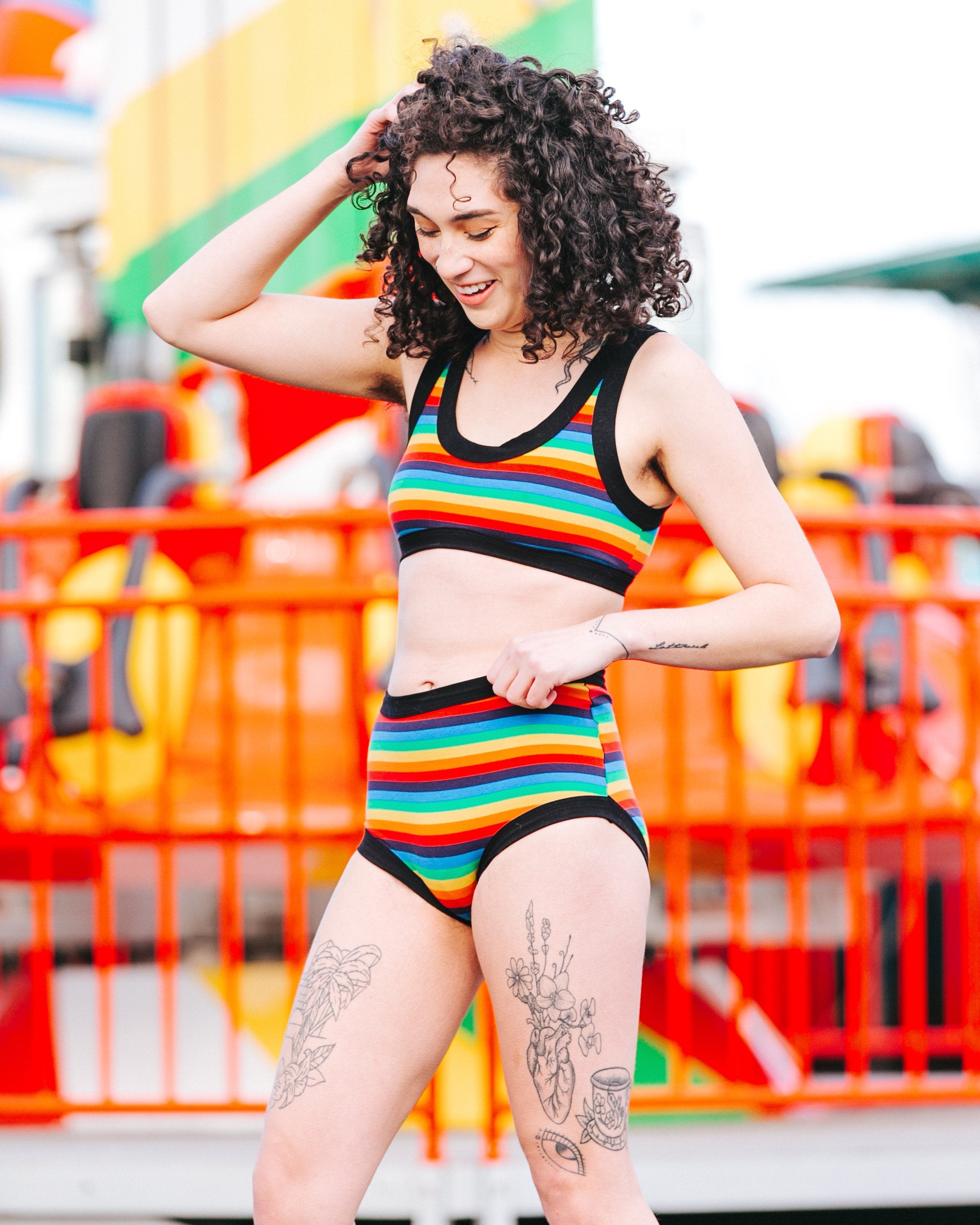 Model smiling at a circus wearing Thunderpants organic cotton Bralette and Original style underwear in rainbow stripes.