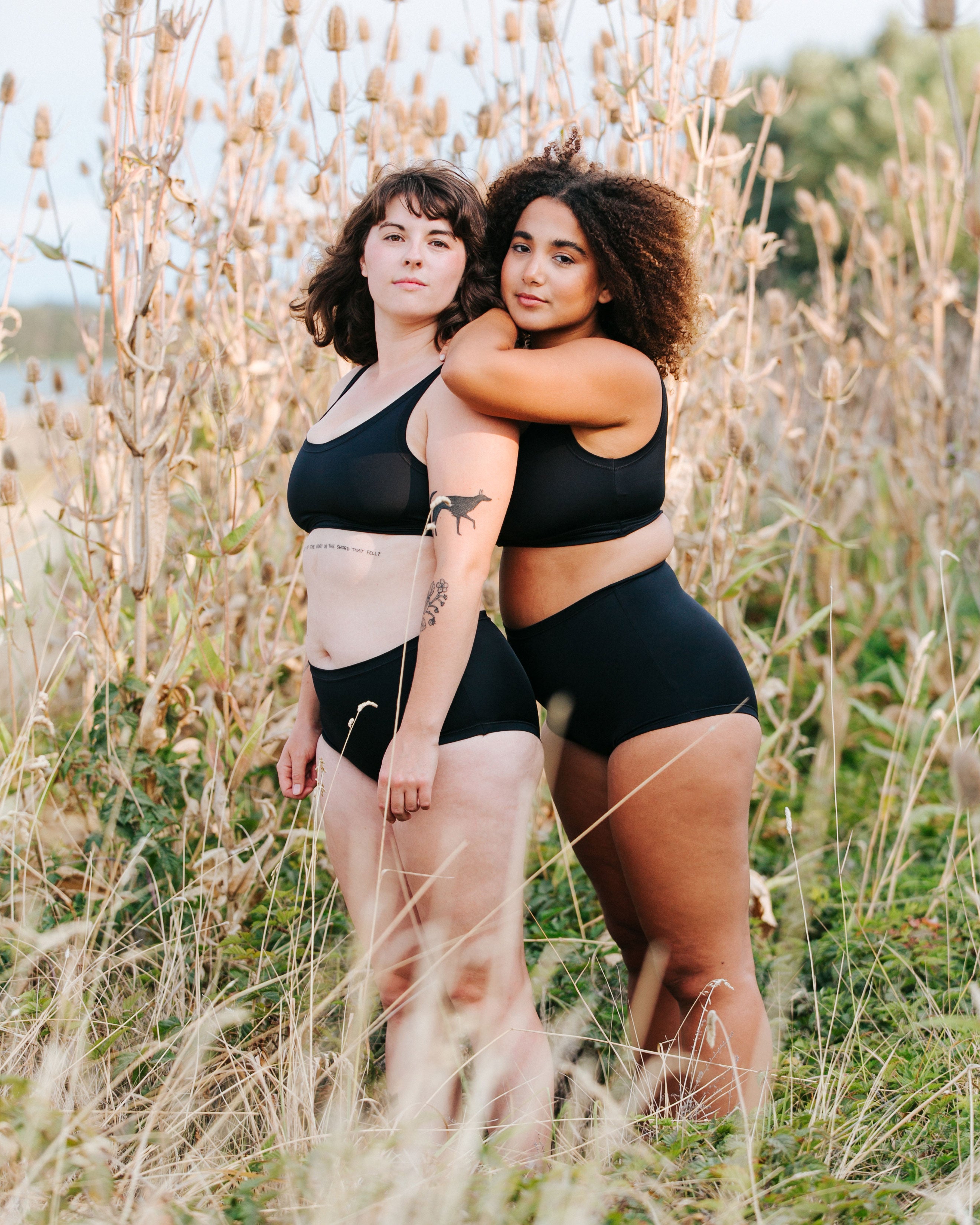 Two models on the beach wearing Thunderpants recycled nylon Original style and Sky Rise style Swimwear Bottoms, and Swimwear Top in Plain Black.