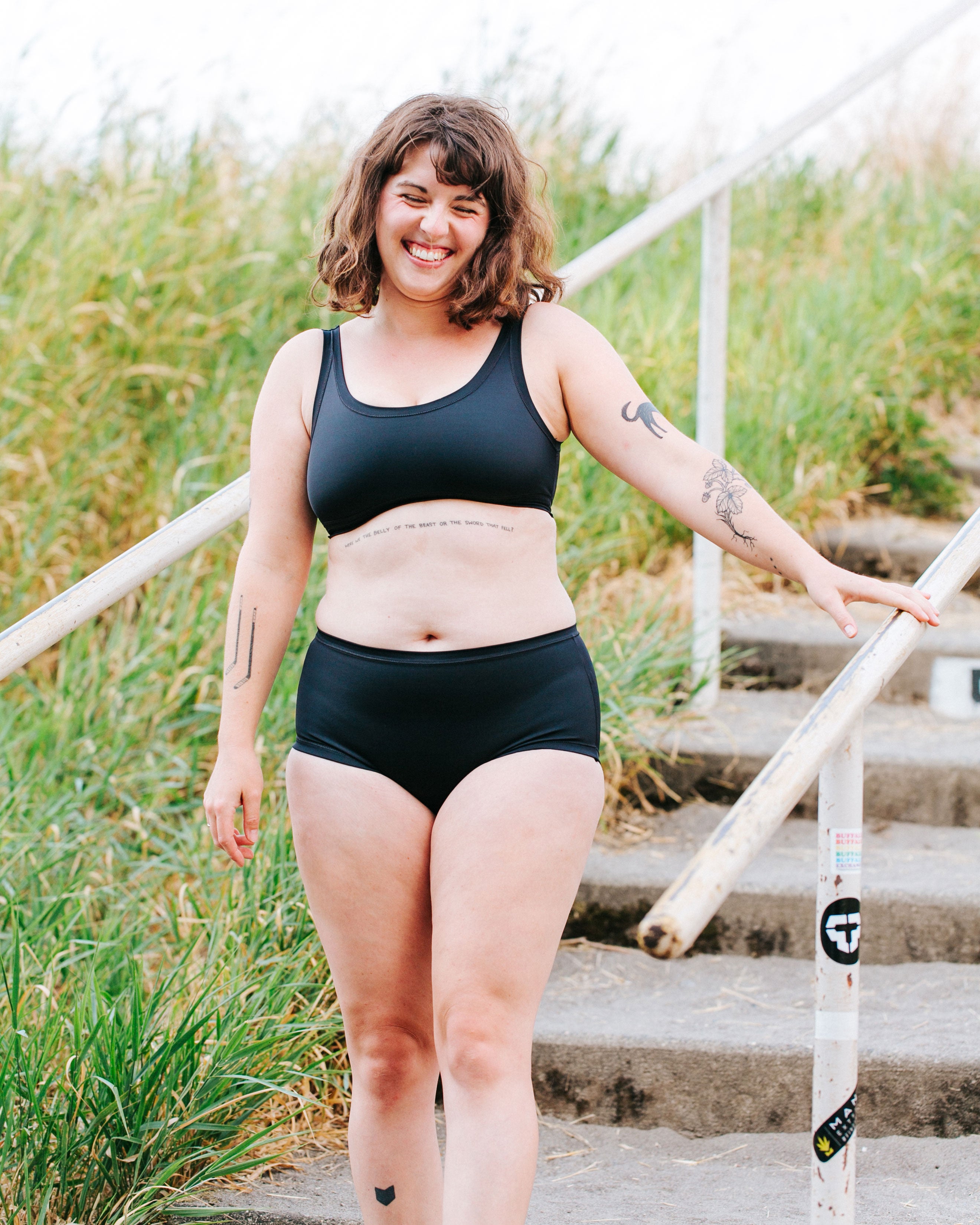 Model standing on stairs and smiling wearing Thunderpants recycled nylon Original style Swimwear Bottoms and Swimwear Top in Plain Black.