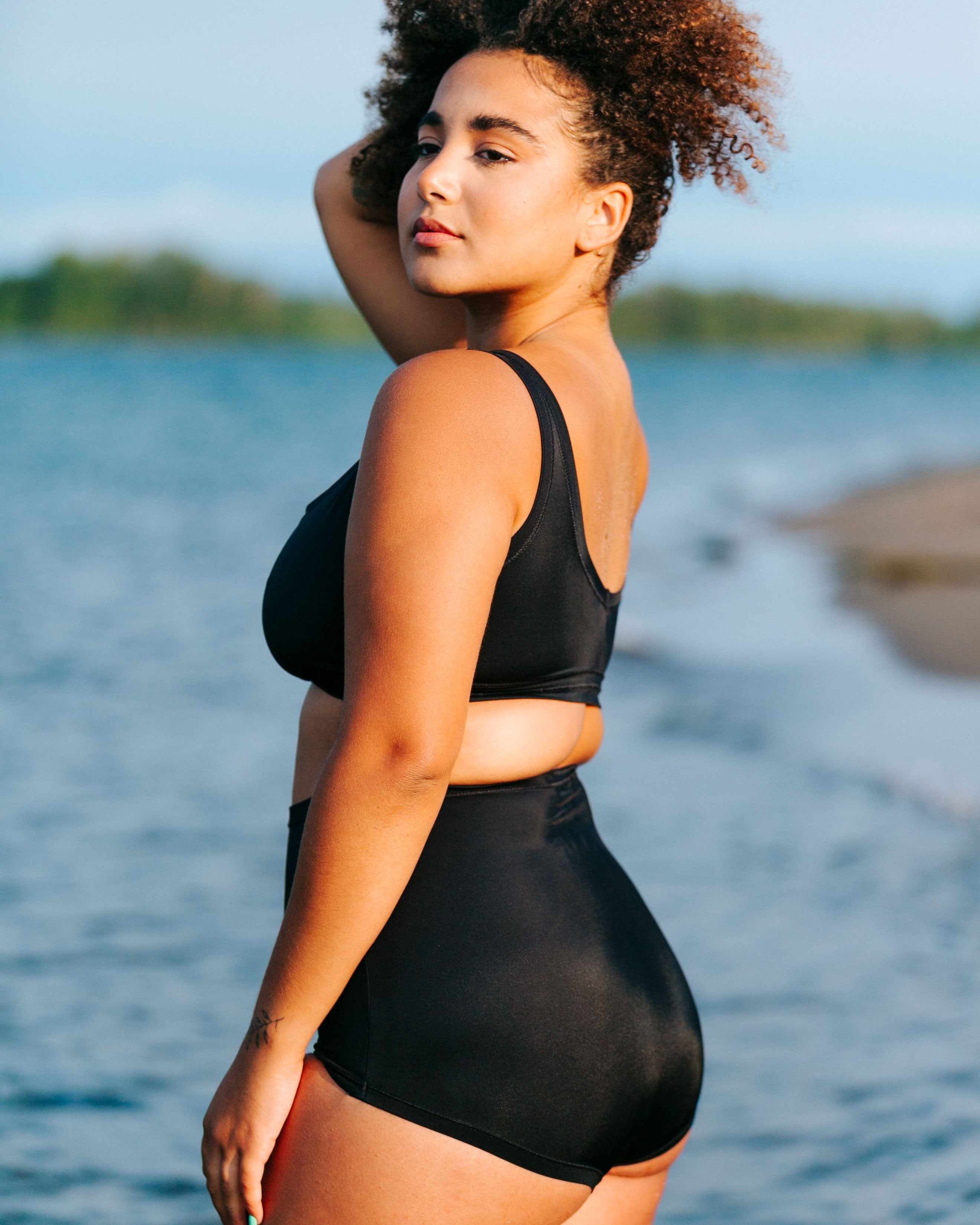 Model standing in the water with back to us wearing Thunderpants recycled nylon Sky Rise style Swimwear Bottoms and Swimwear Top in Plain Black.