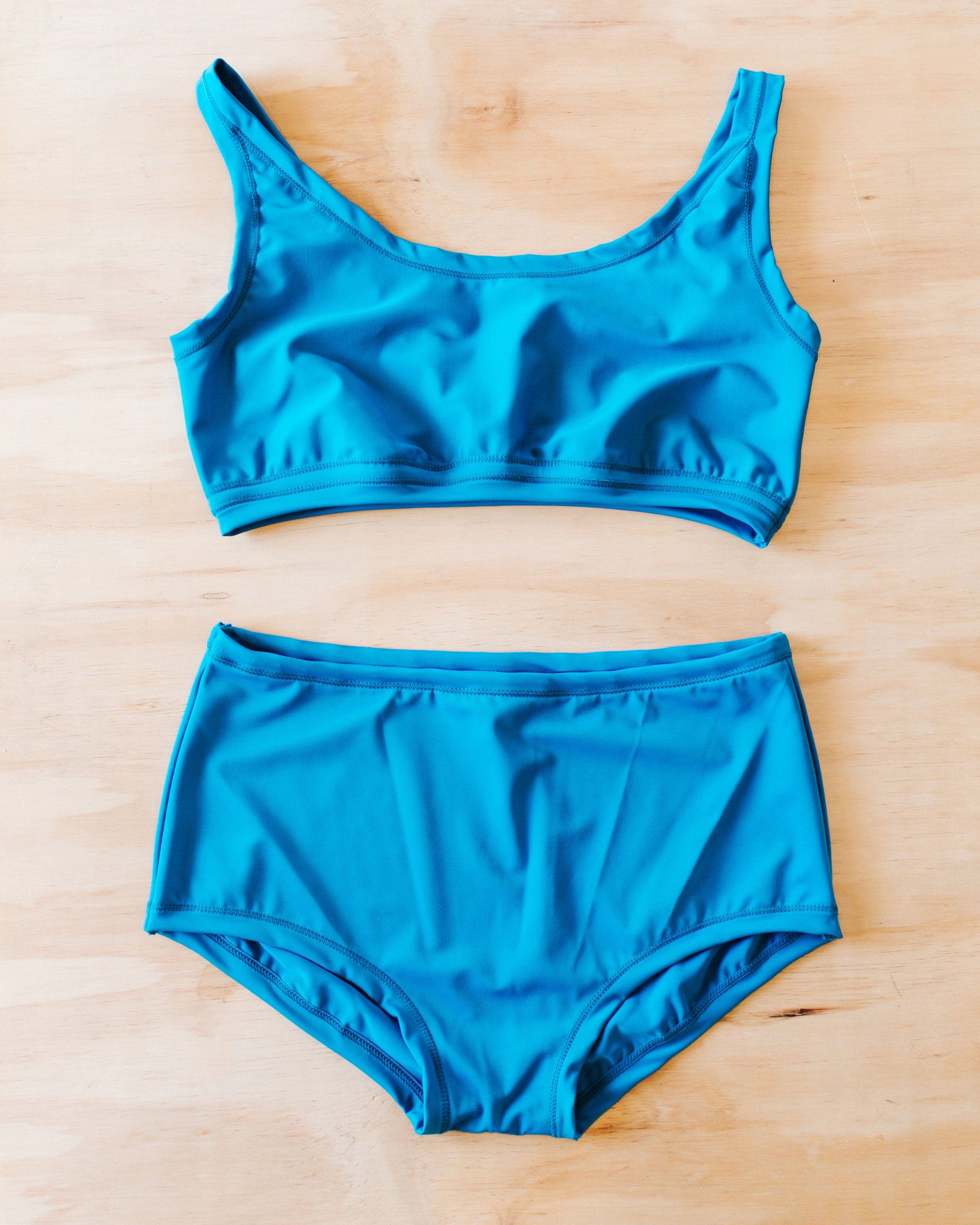 Flat lay on wood surface of Swimwear set with Original style bottoms and top in Marina Blue.