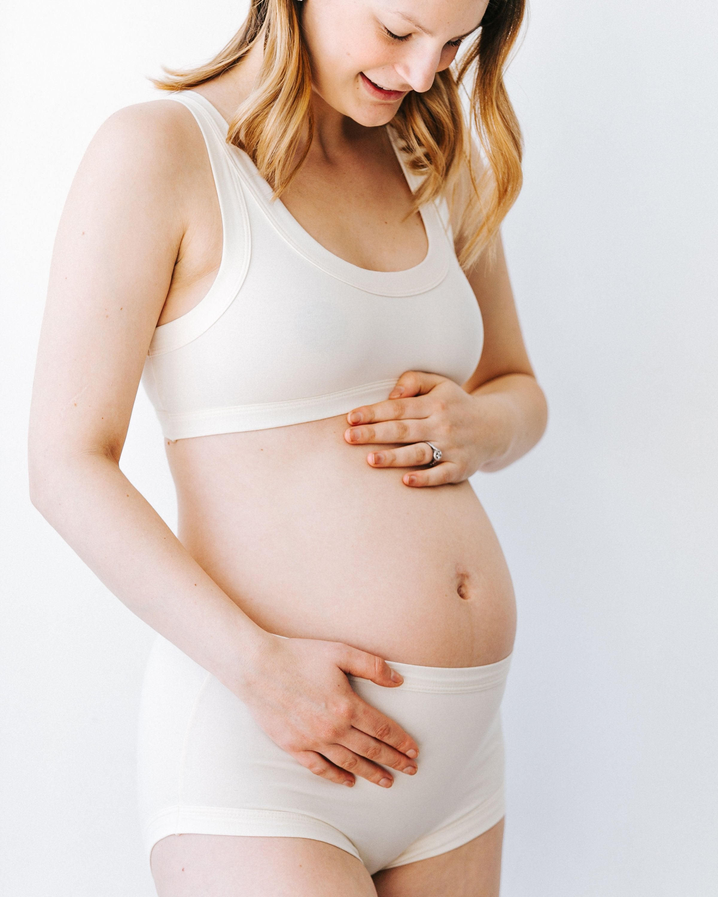 Close up of pregnant model holding her stomach wearing Thunderpants organic cotton Original style underwear and Bralette in plain off-white Vanilla.