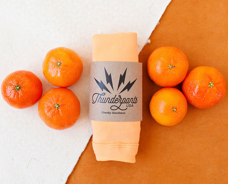 Flat lay of a packaged pair of Orange Sherbet underwear on a white and orange surface with oranges around it.