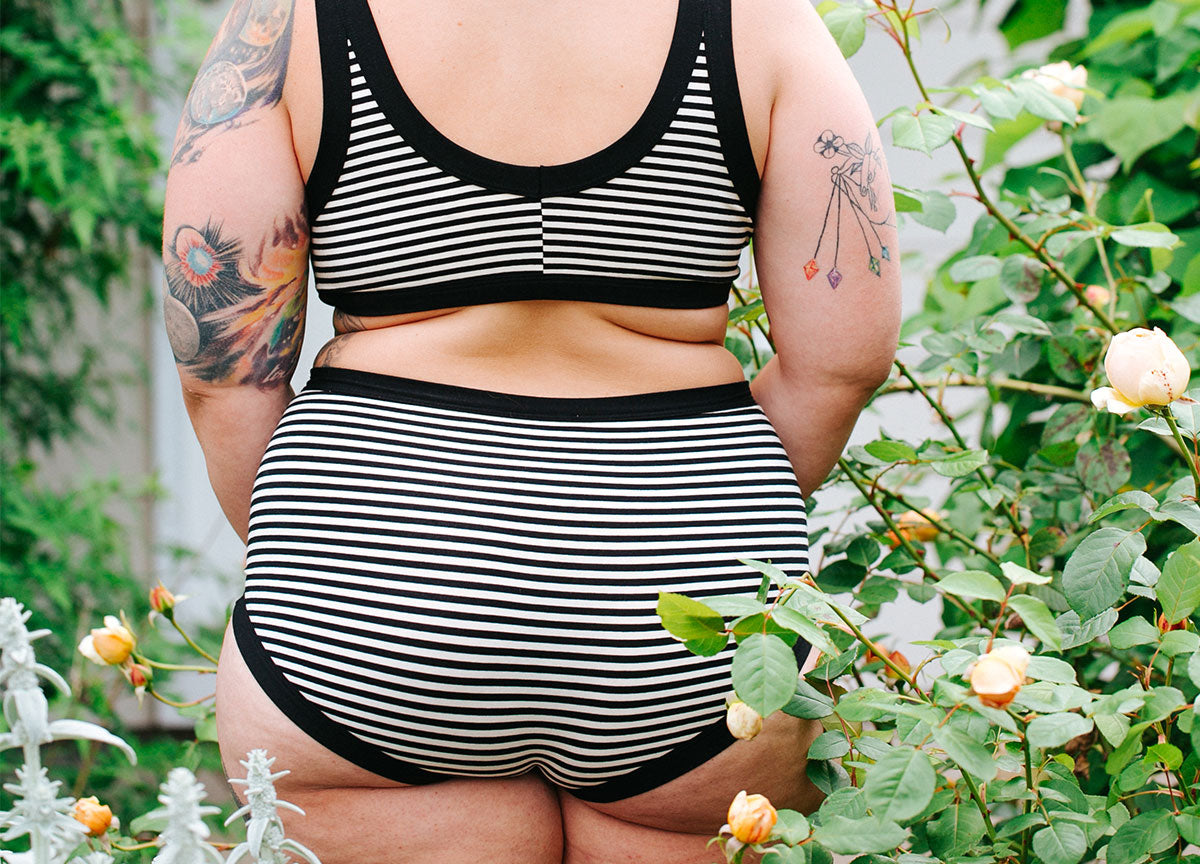 Women standing in roses with her back to the camera wearing Thunderpants Original style underwear and Bralette in Black and White Stripes.