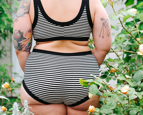 Women standing in roses with her back to the camera wearing Thunderpants Original style underwear and Bralette in Black and White Stripes.