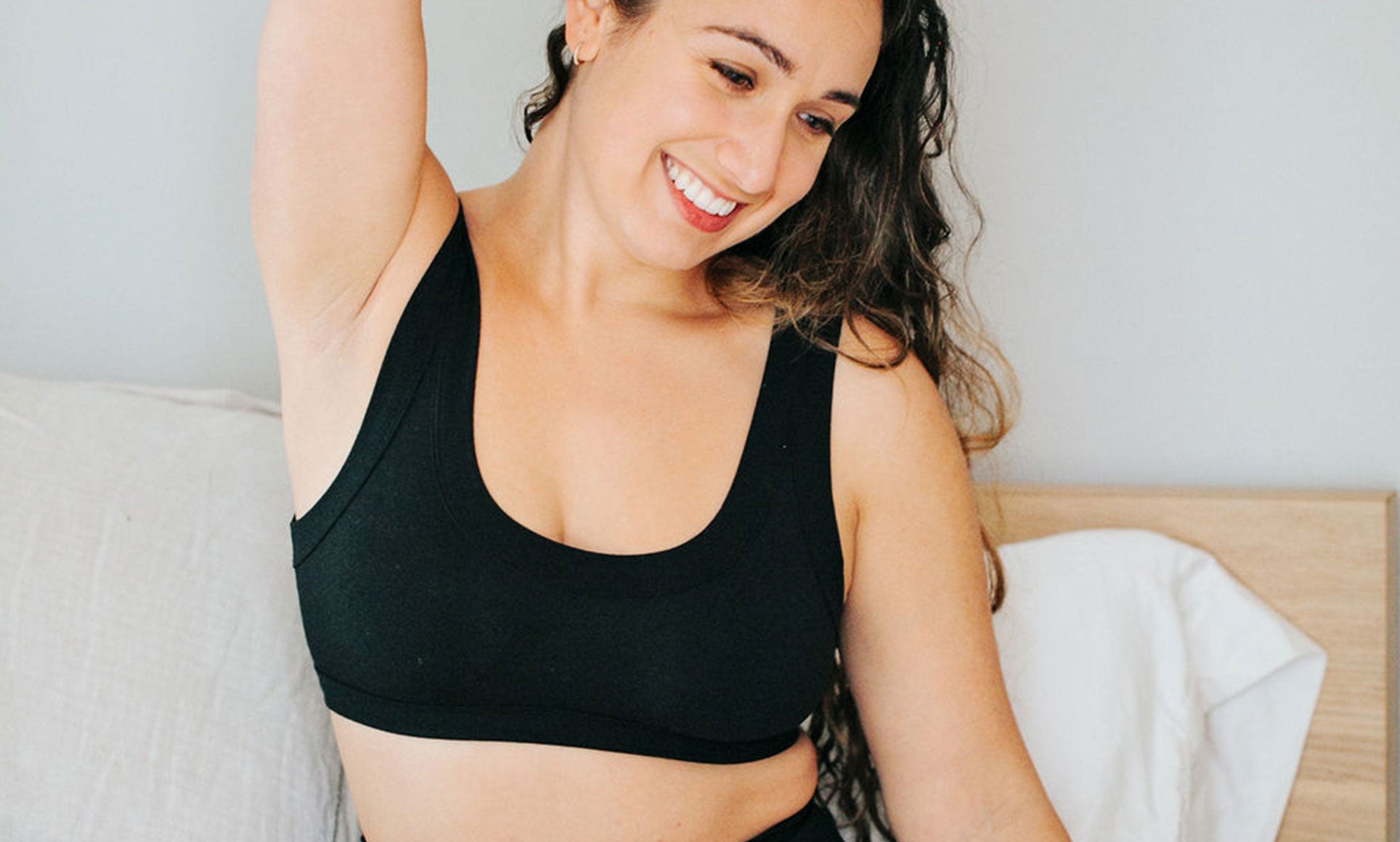 Model smiling while sitting on a bed wearing Thunderpants Bralette in Plain Black.