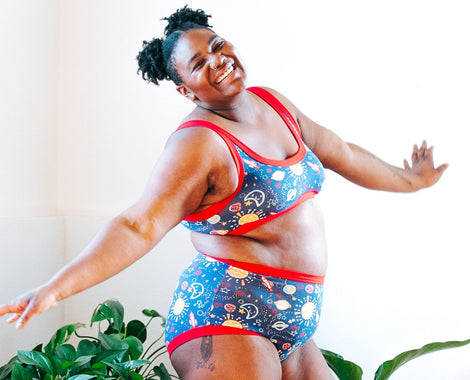 Woman smiling with joy wearing Thunderpants Organic Cotton Underwear and Bralette in our Dark Sky Print: dark blue with colorful planets and red binding.