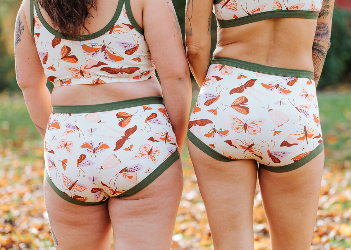 Two models wearing Thunderpants Original and Sky Rise style underwear in Field Day: moths in pink, red, and purple with green binding.