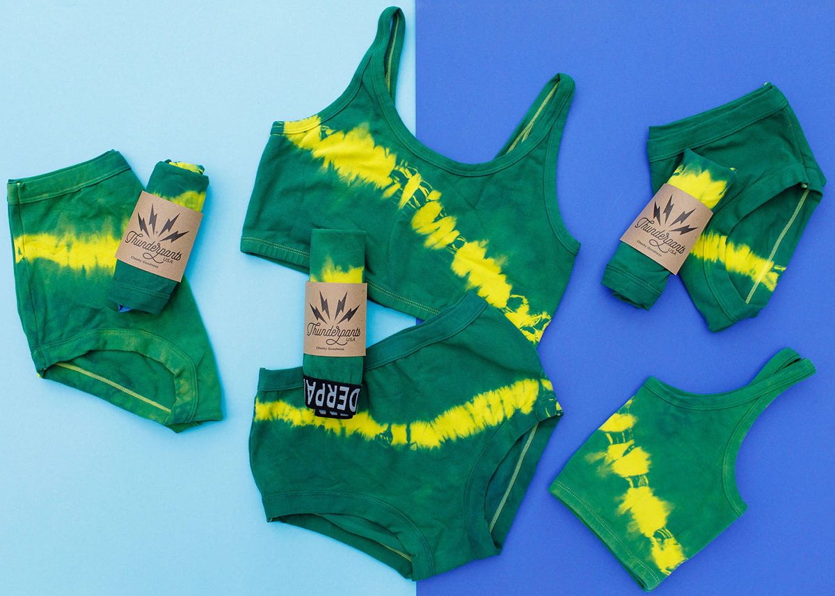 Flat lay of multiple Thunderpants styles in Lightning Bolt hand dye - blue/green with yellow stripe.