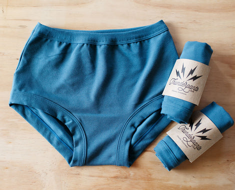 Flat lay of Thunderpants Organic Cotton Original underwear with two packaged underwear in Stormy Blue: a beautiful darker blue color.