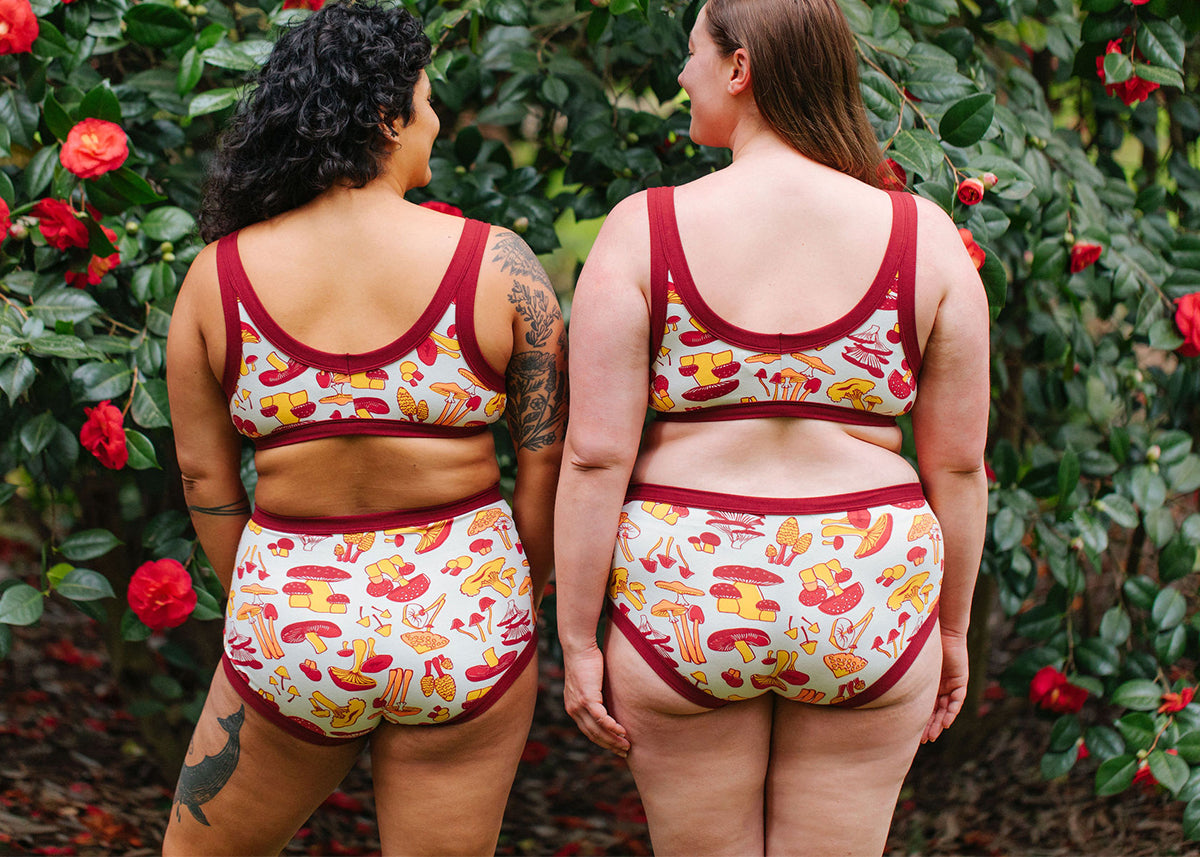 Two models wearing Thunderpants Bralette and Original style underwear sets in Whadda Mushroom - red, orange, and yellow mushroom print.