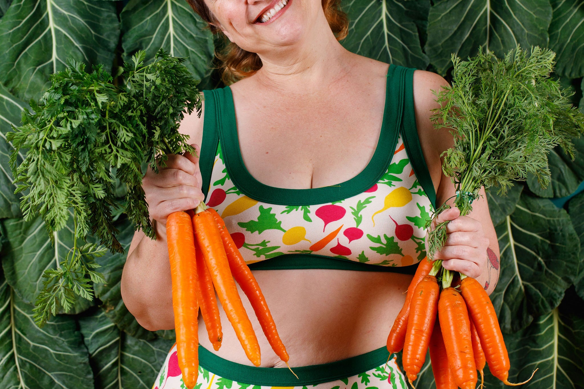 Model holding two bunches of carrots wearing Thunderpants Sky Rise style underwear and Bralette in Root Veggies.