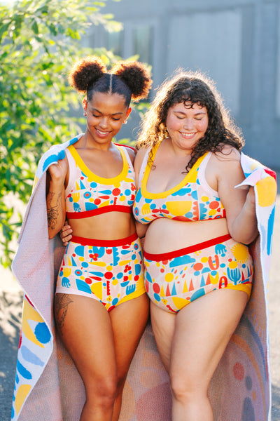 Two people smiling together wearing Thunderpants Original, Sky Rise, and Bralette in Balance by Lisa Congdon print (colorful shapes).