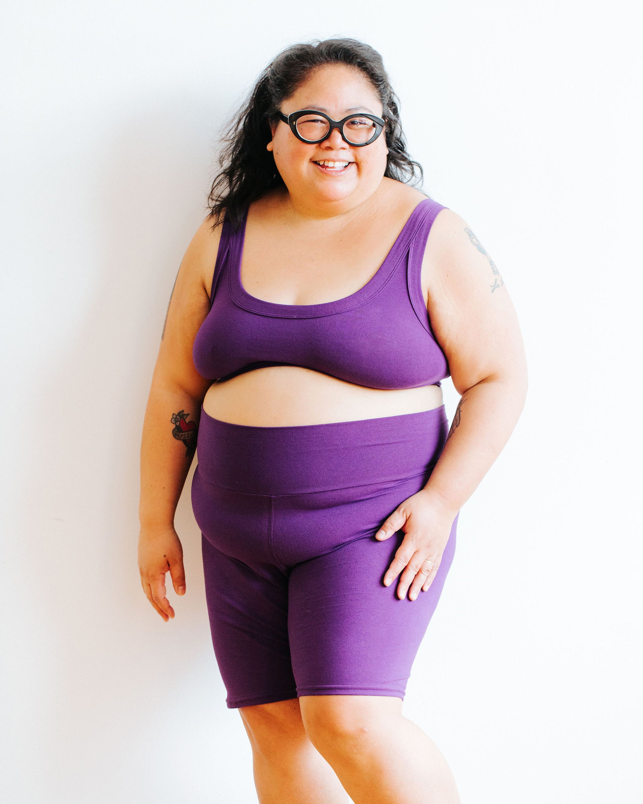 Model smiling while wearing a Bralette and Bike Shorts both in Deep Amethyst.